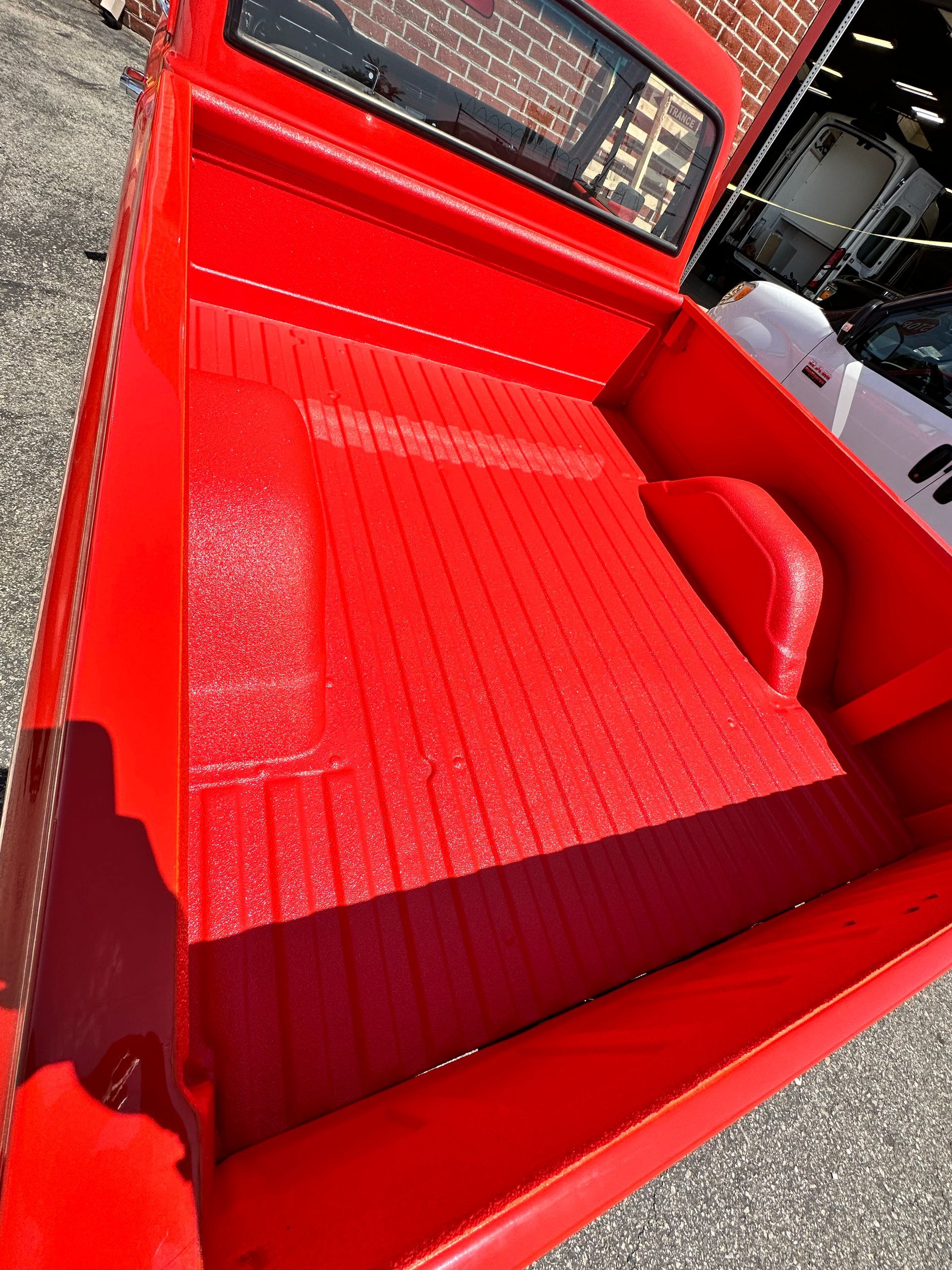 The empty, bright red truck bed of a vintage pickup truck features a textured, coated floor and wheel wells.