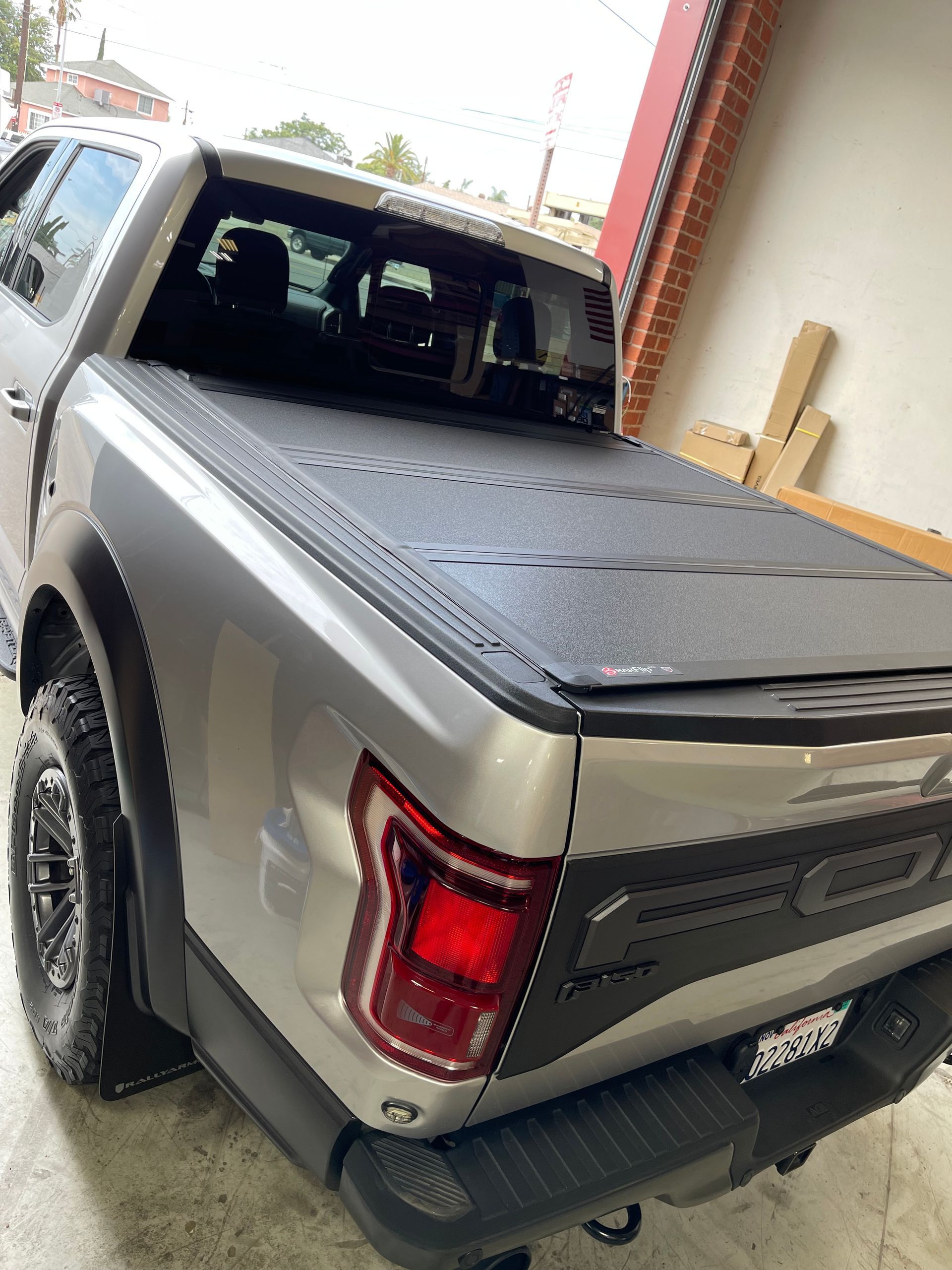 A silver Ford F-150 Raptor pickup truck with a black folding tonneau cover parked indoors.