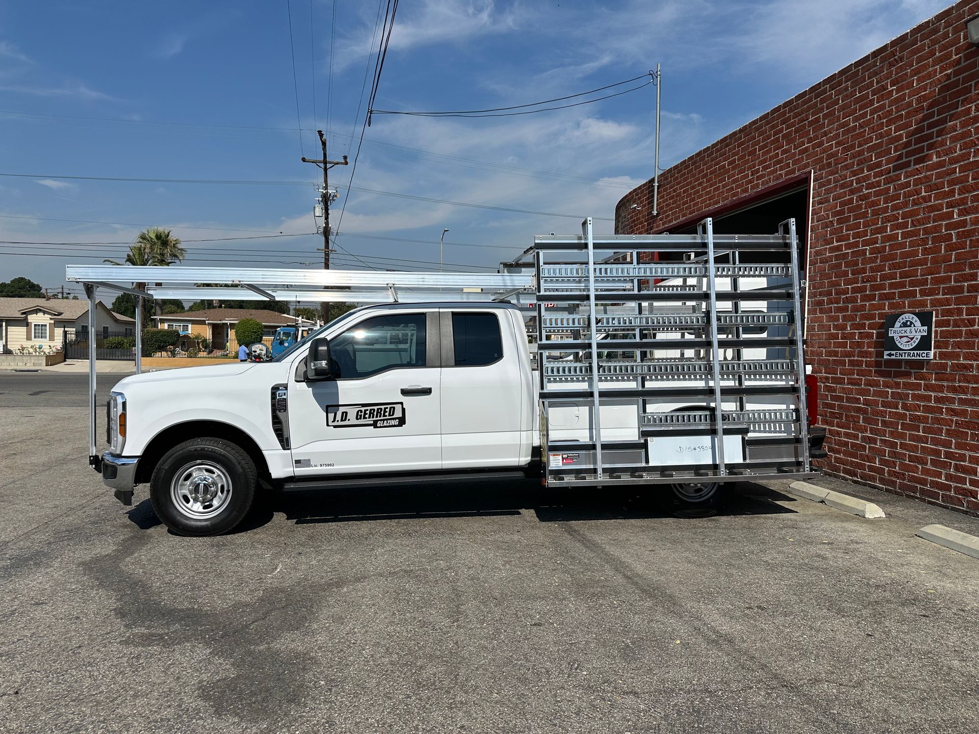 A white Ford Super Duty truck parked outside a brick building, featuring an extensive roof and side rack system.