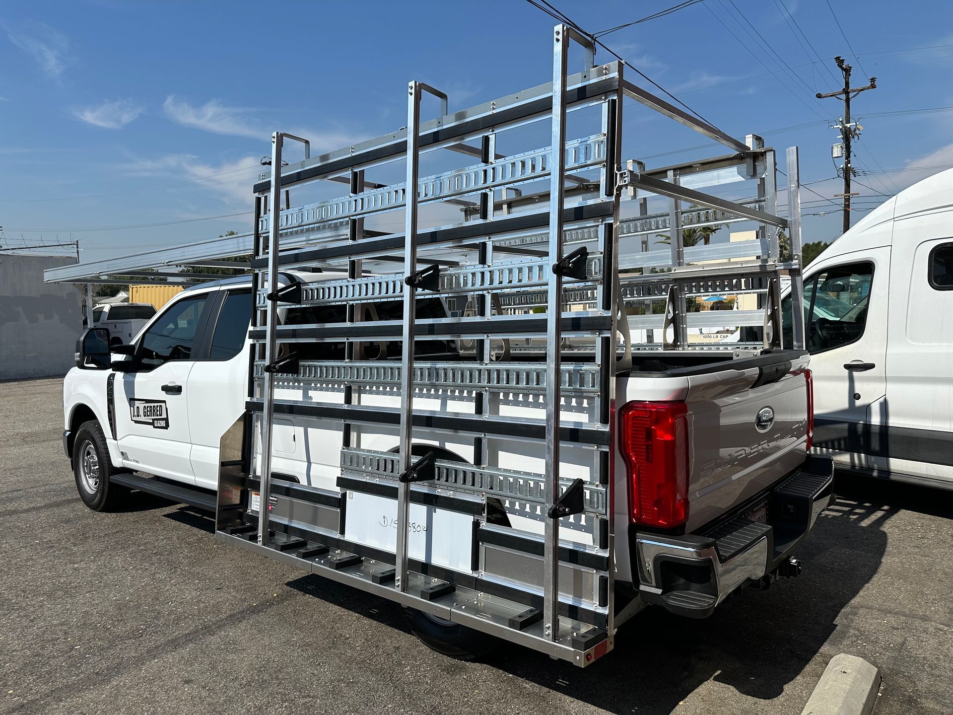 A white pickup truck parked outdoors, featuring a large metal glass-carrying rack attached to its passenger side.
