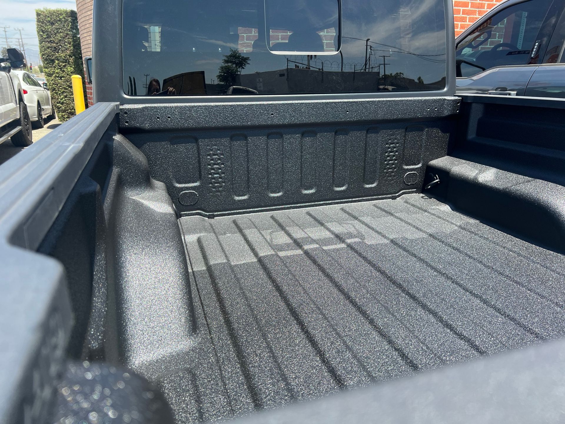 Empty pickup truck bed with a textured black spray-in bed liner, viewed from an angled perspective.
