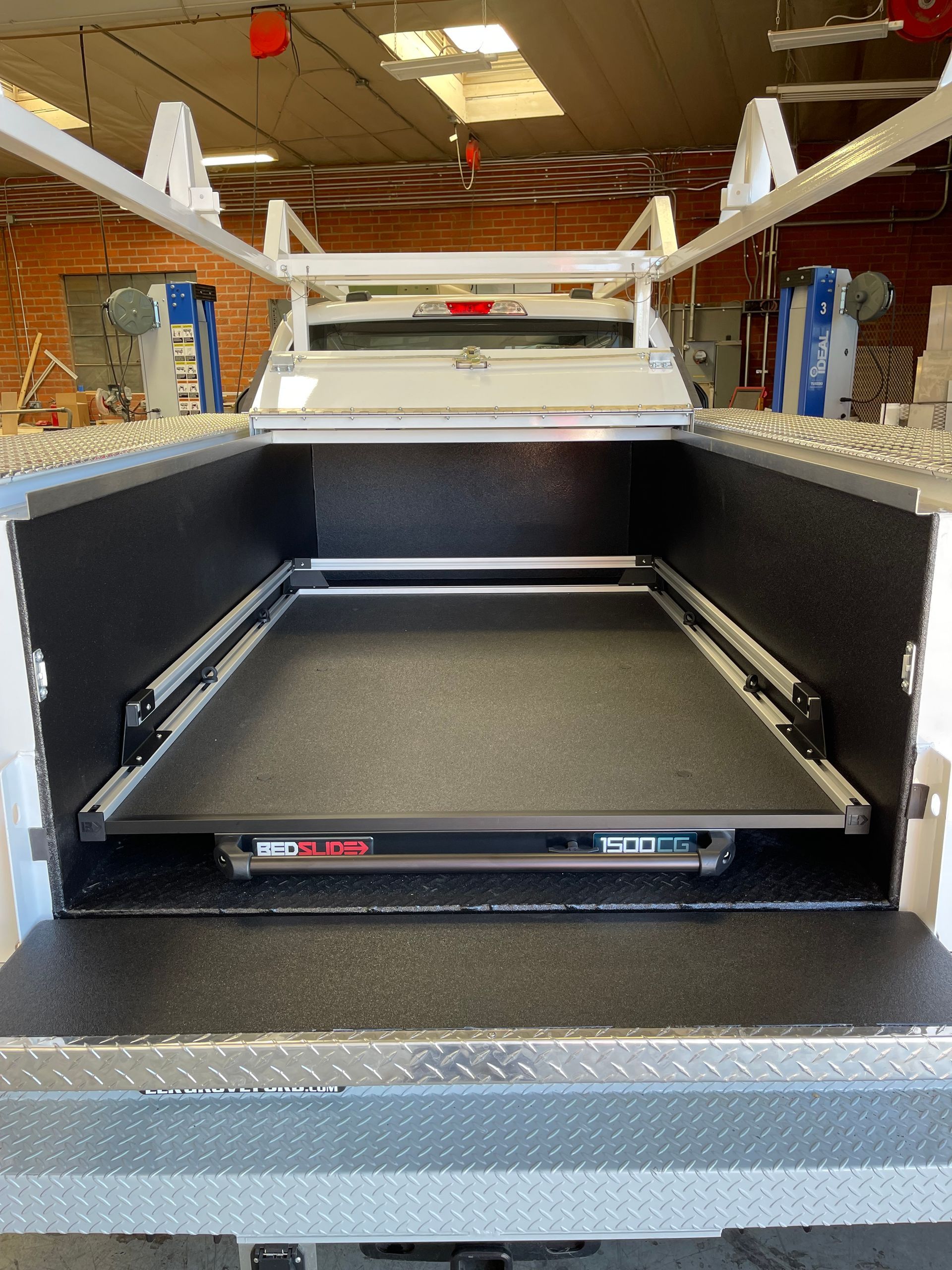 Open bed of a pickup truck featuring a black sliding cargo tray, a ladder rack, and diamond-plate metal trim.