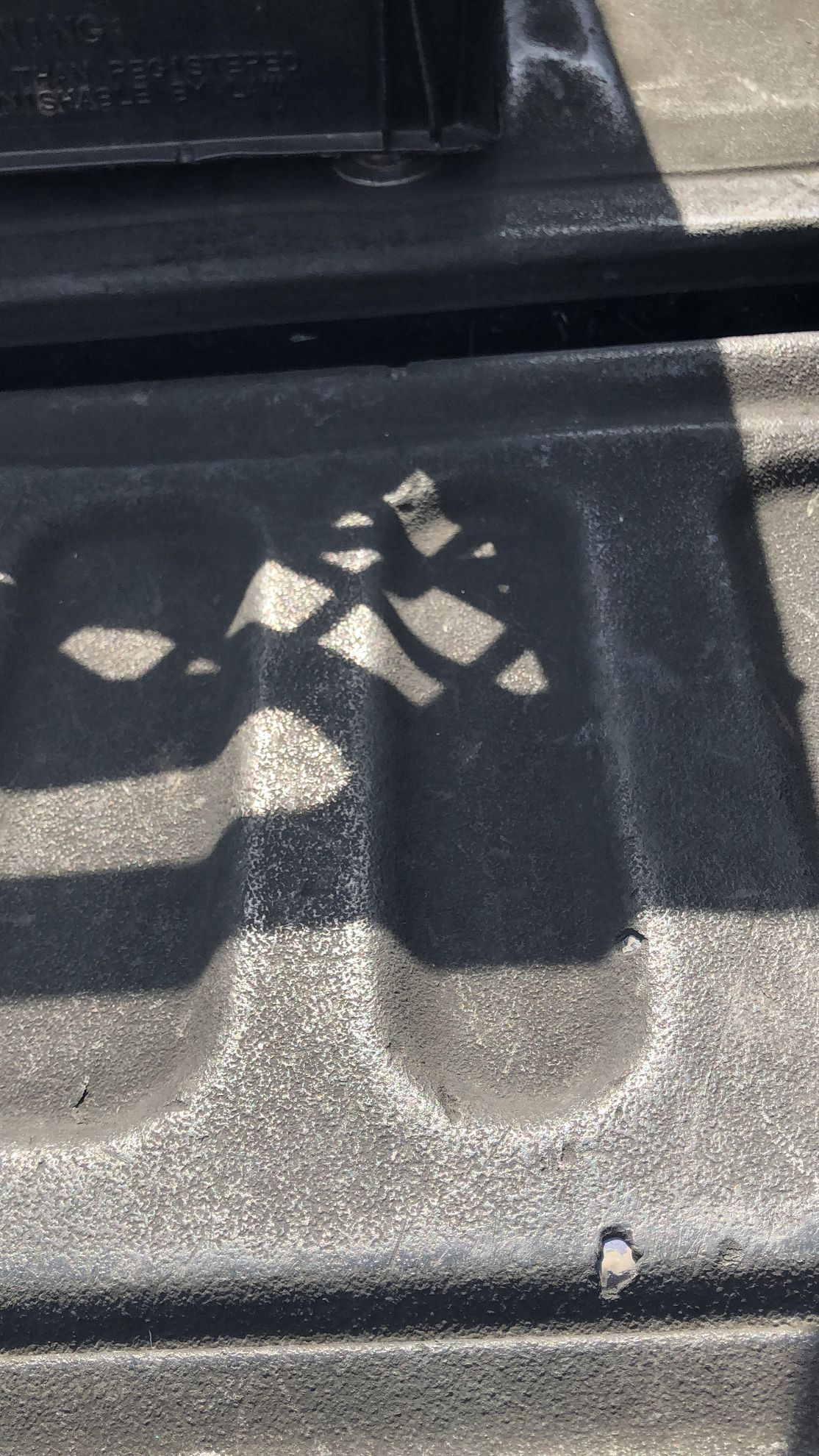 Shadow of a checkered flag cast onto a textured, black truck bed liner.