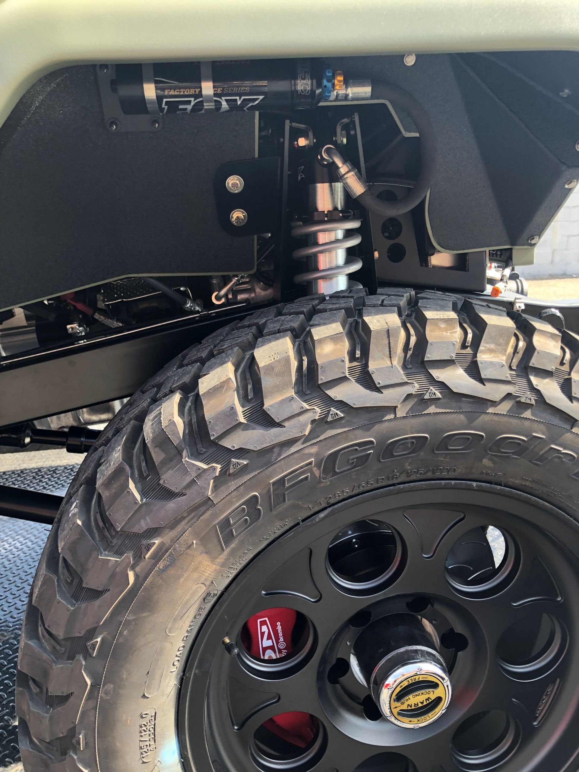 A close-up of a vehicle's suspension system featuring a coil-over shock with a remote reservoir, tire, and wheel.