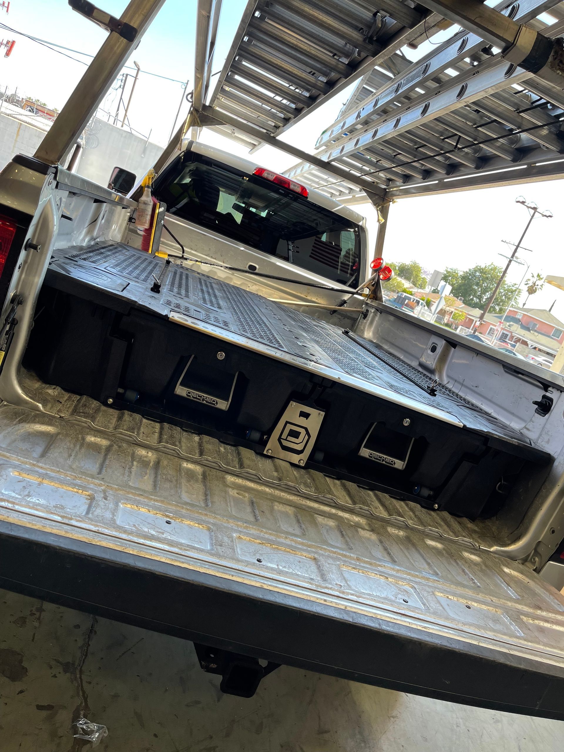A black storage drawer system installed in the bed of a pickup truck with a roof ladder rack.