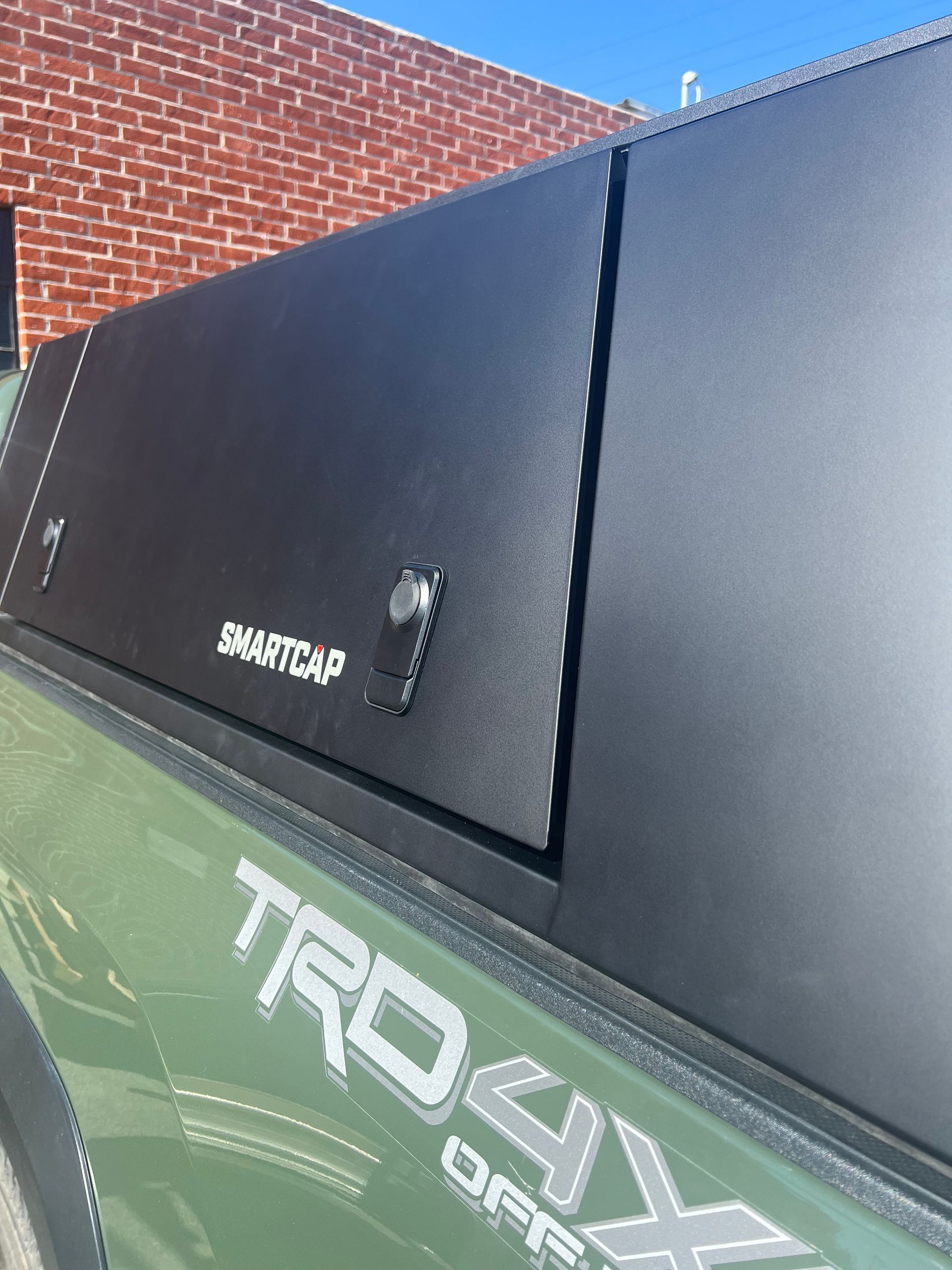 Close-up of a matte black RSI SmartCap truck topper mounted on an army green Toyota Tacoma TRD Off-Road pickup truck.