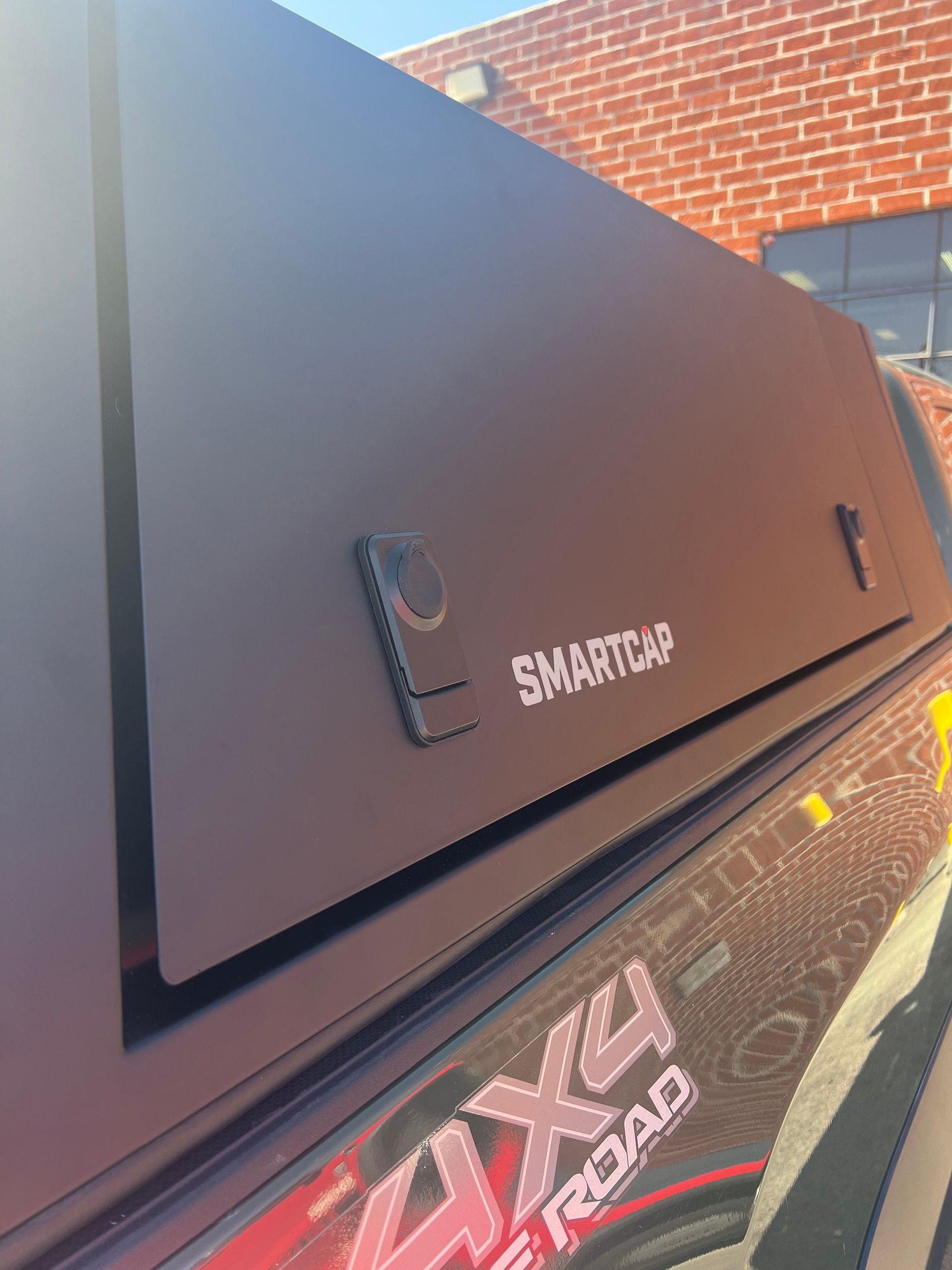 Close-up of a matte black SmartCap truck bed topper with a locking handle, mounted on a 4x4 off-road vehicle.