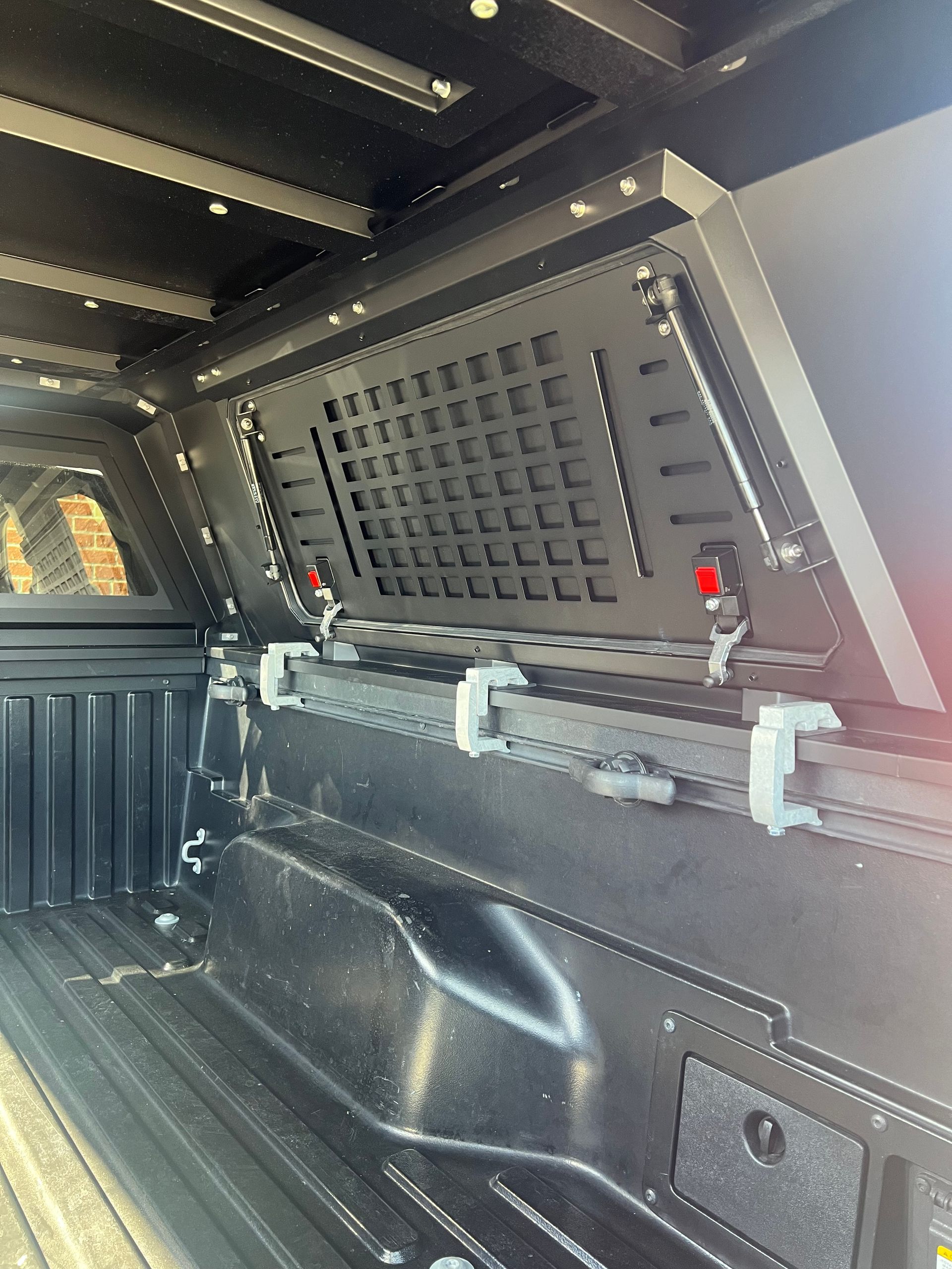 Black metal MOLLE grid panel mounted inside the bed of a truck, featuring integrated rail attachments.