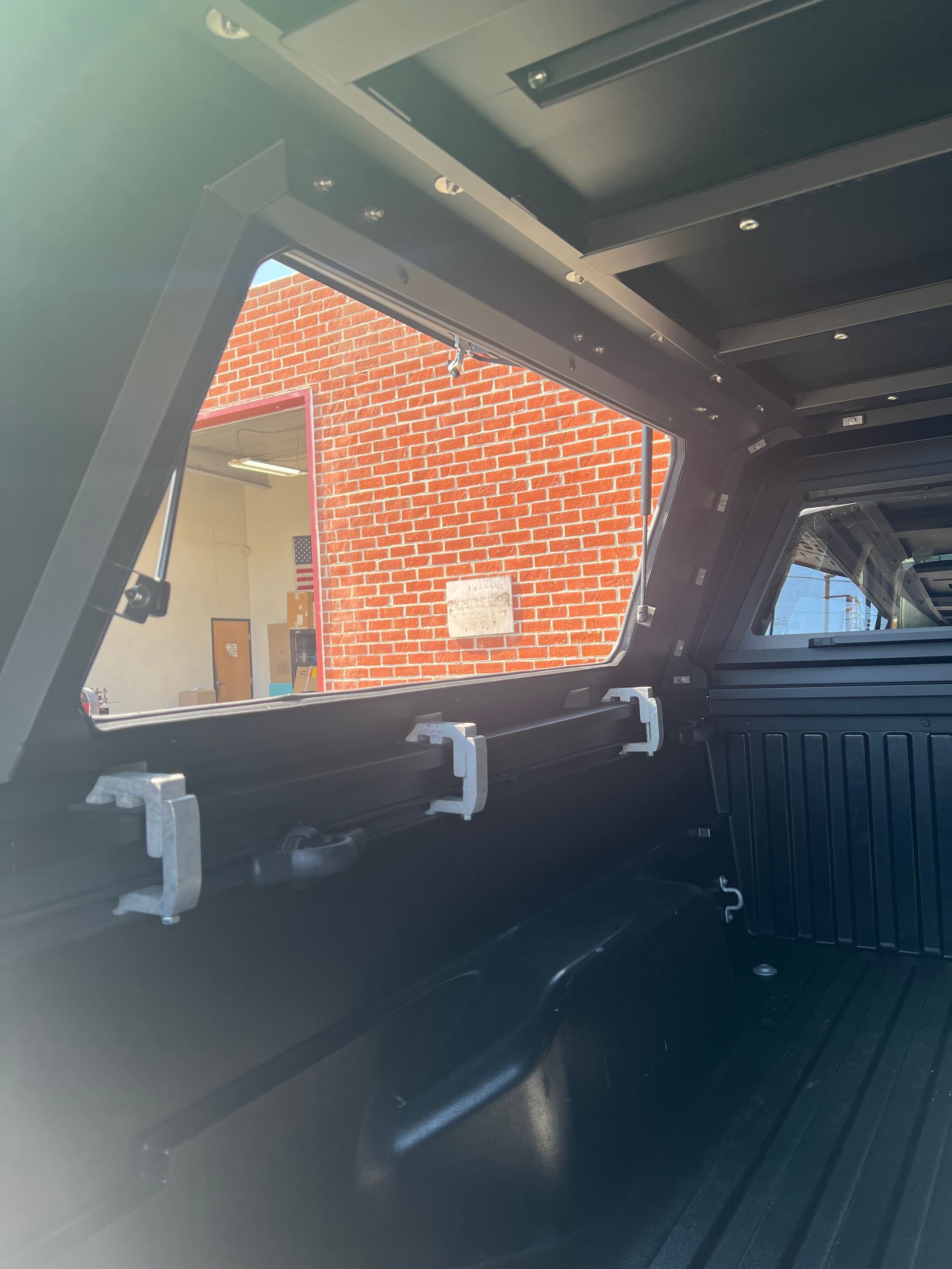 Interior view of a truck bed with a black canopy, showing a window looking out onto a red brick building.