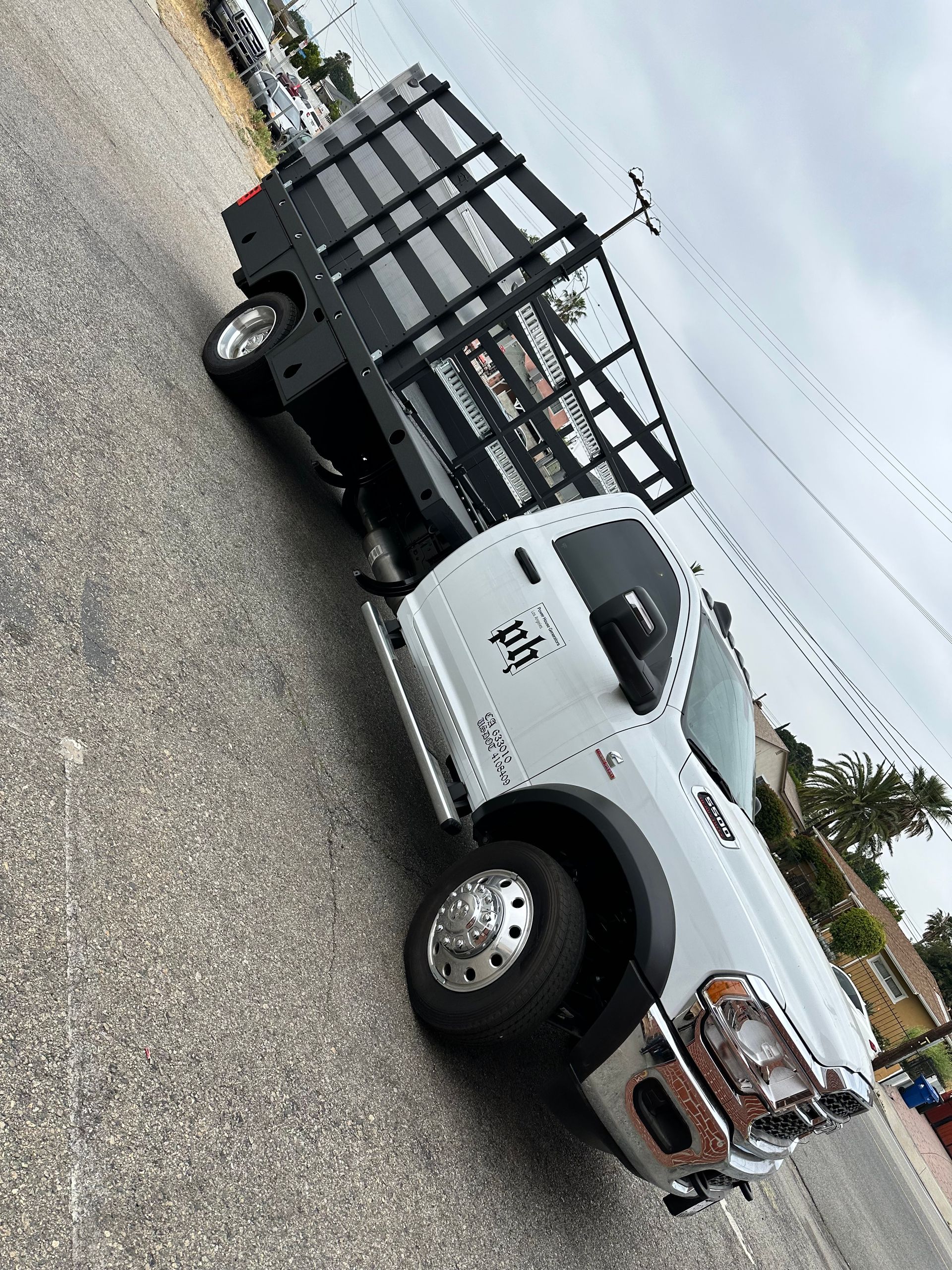 A white work truck with a large black stake-body trailer parked on a paved lot.