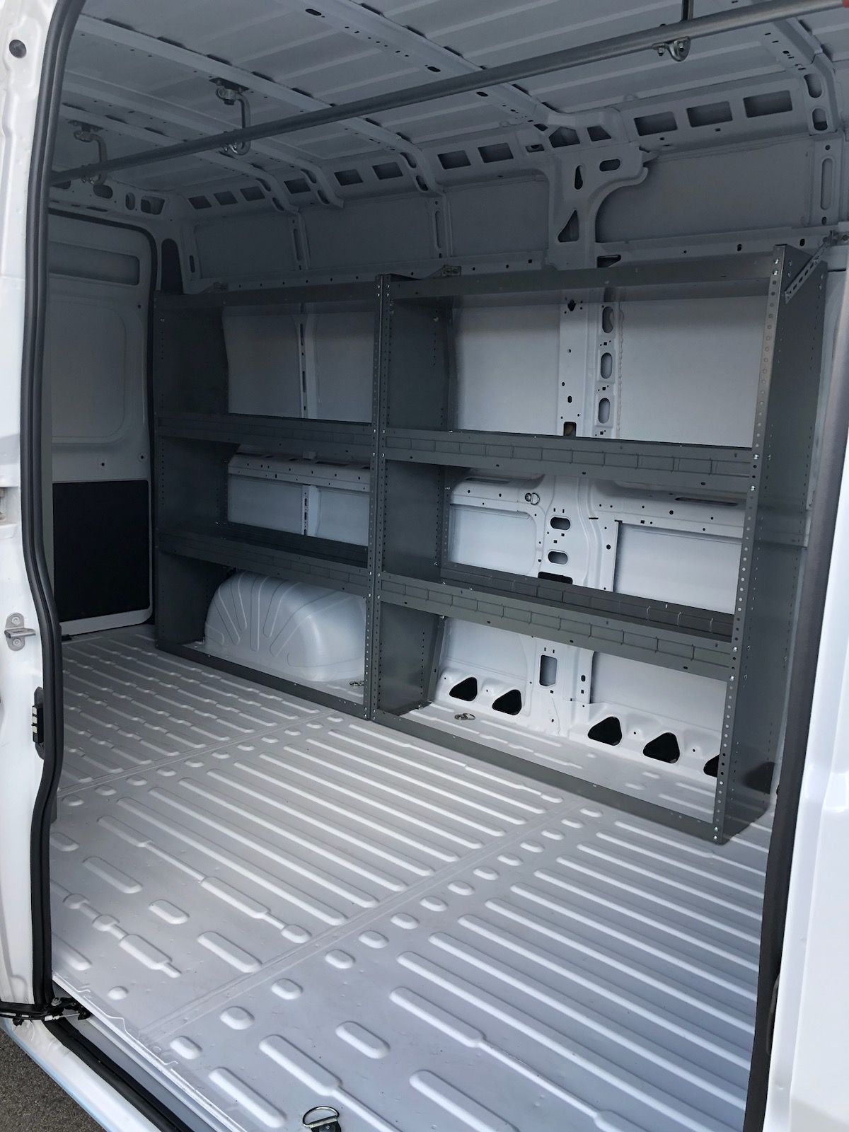 The cargo area of a white van with grey metal shelving units installed along the side and a light-colored floor.