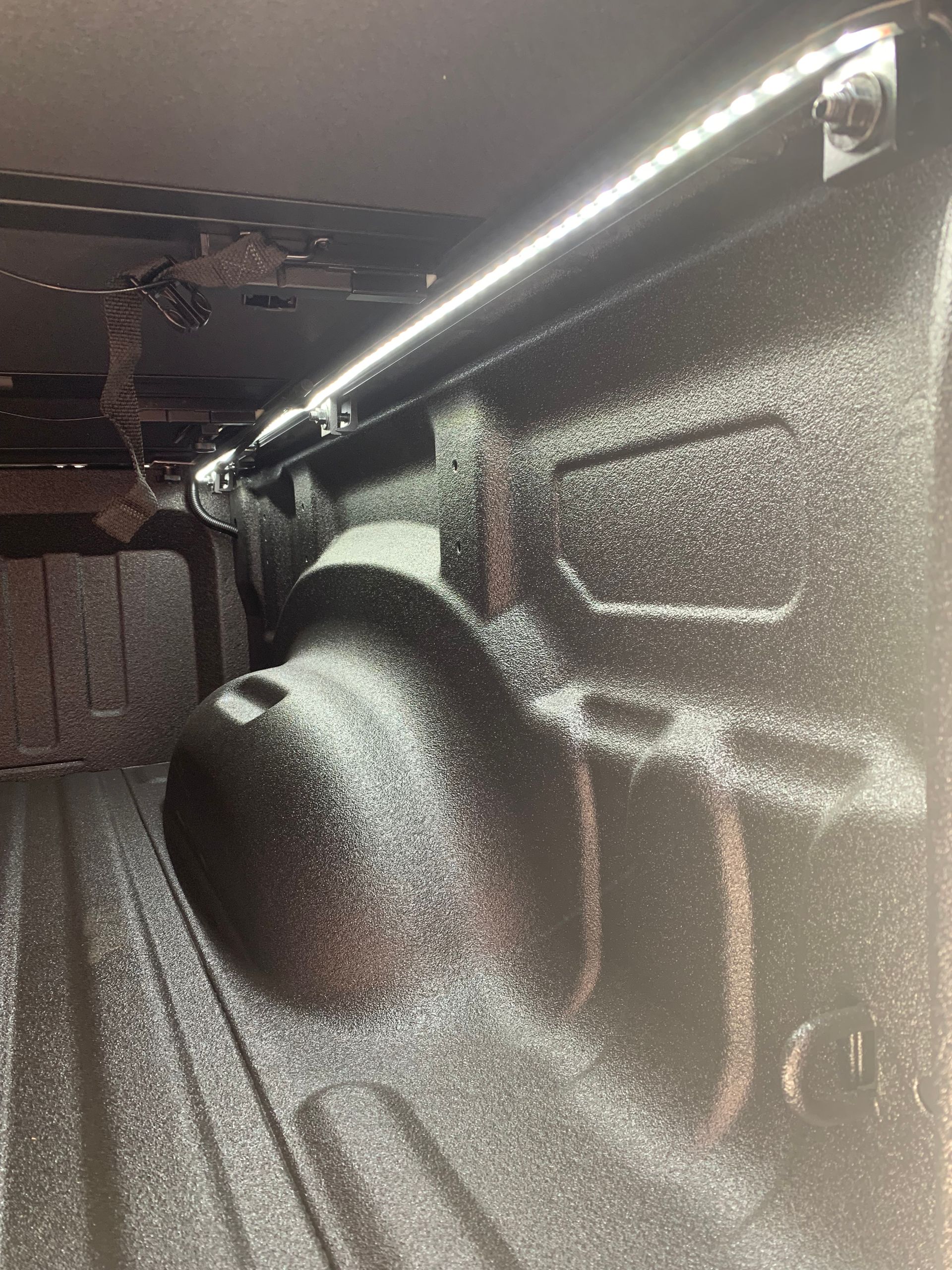 An LED strip light mounted along the interior rim of a black spray-in truck bed liner.