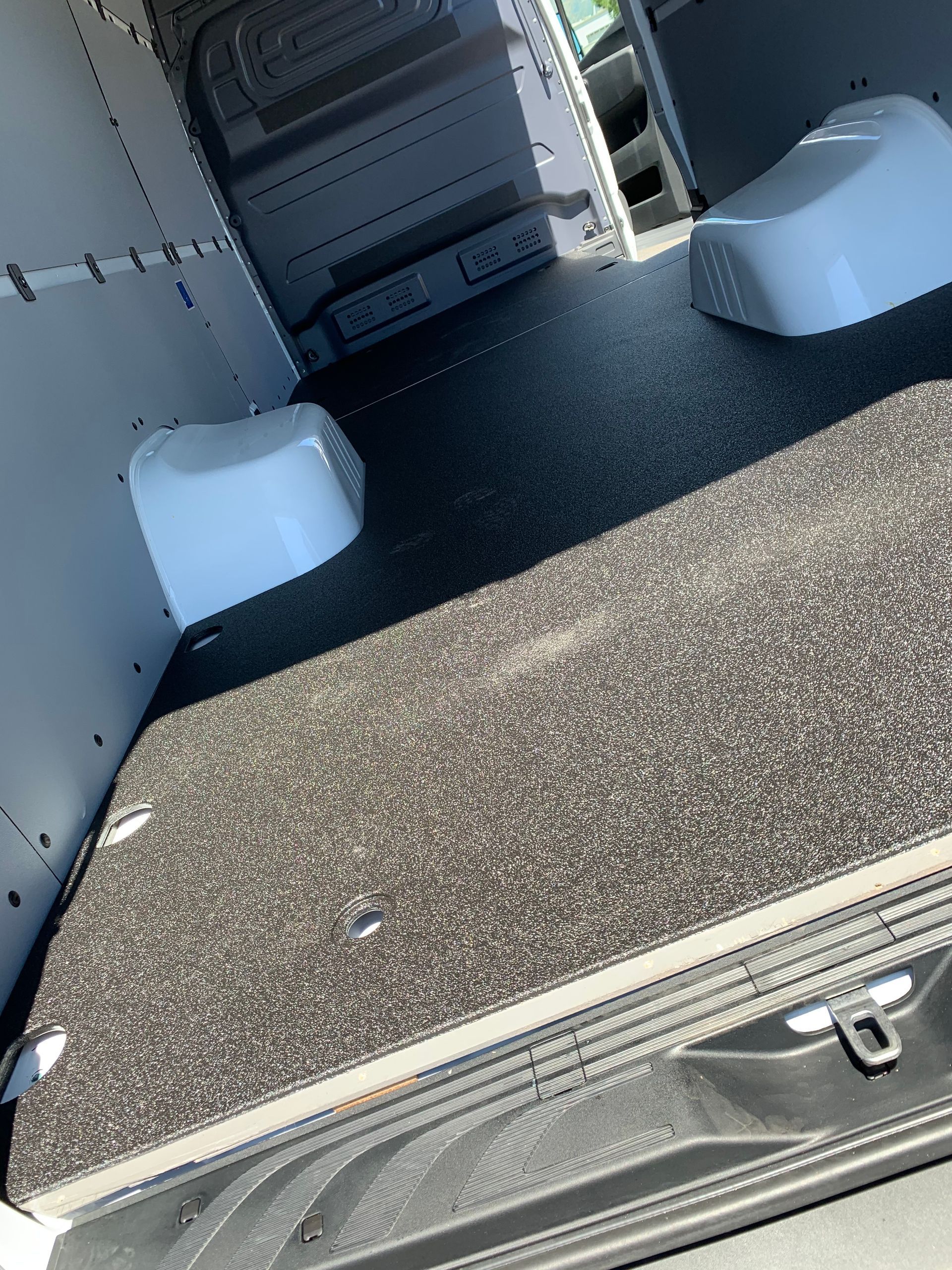 Interior view of a cargo van with a carpeted floor, white wheel wells, and light-colored metal side panels.