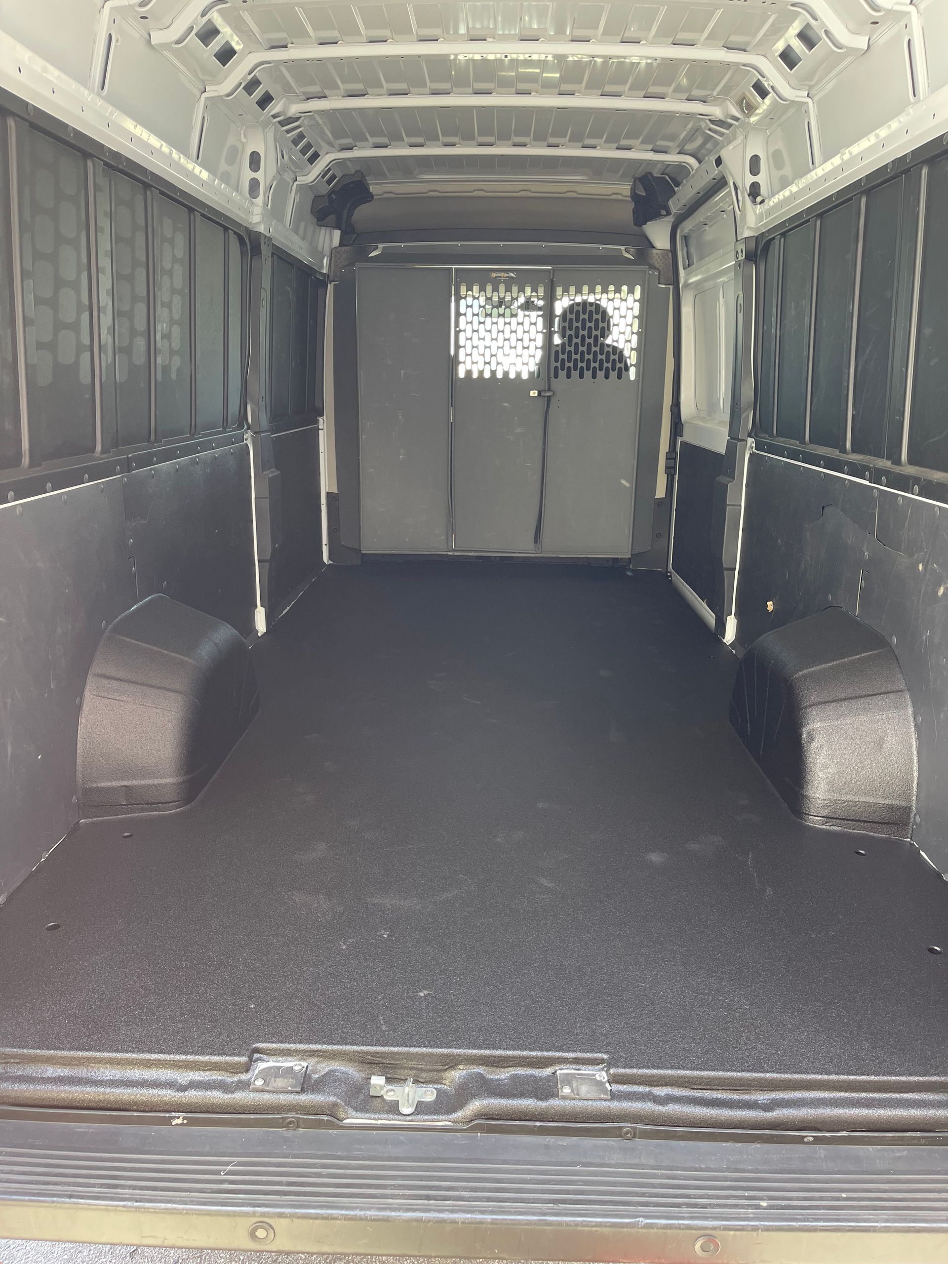 The interior of an empty cargo van, featuring dark grey textured walls and flooring with a metal partition in the back.