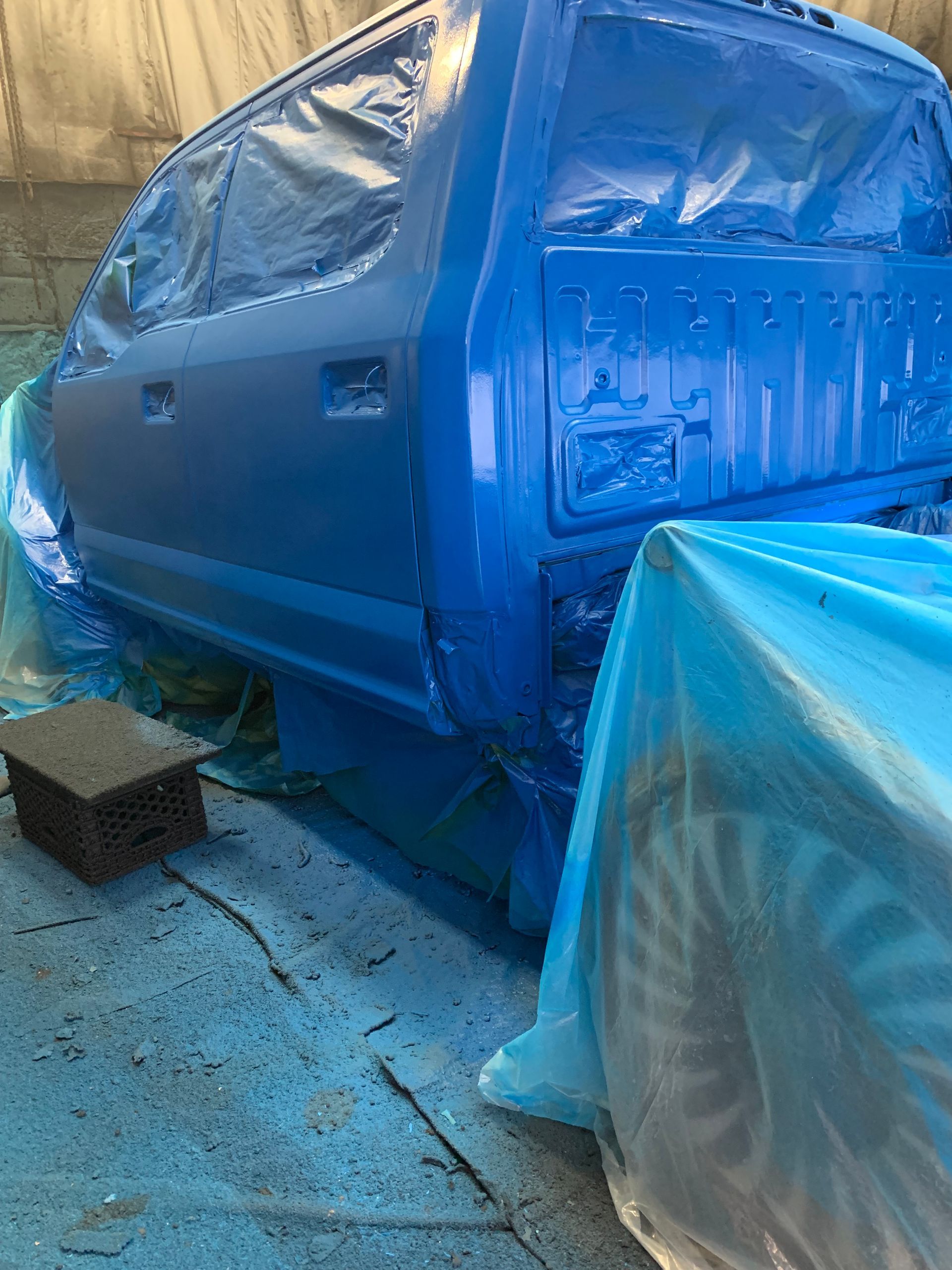 A truck body in a shop, masked with plastic sheeting and freshly painted in a vibrant, uniform bright blue.