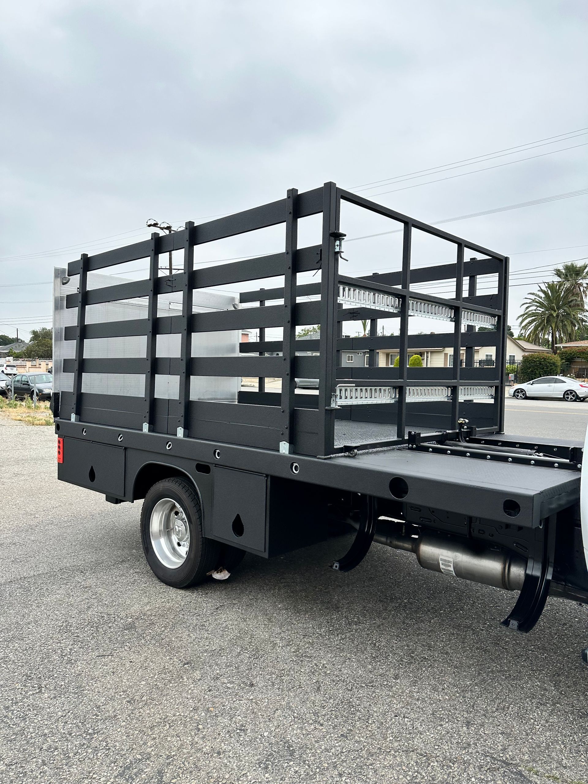 A black flatbed truck with a high wooden slatted cargo cage, parked on a gravel lot under a cloudy sky.