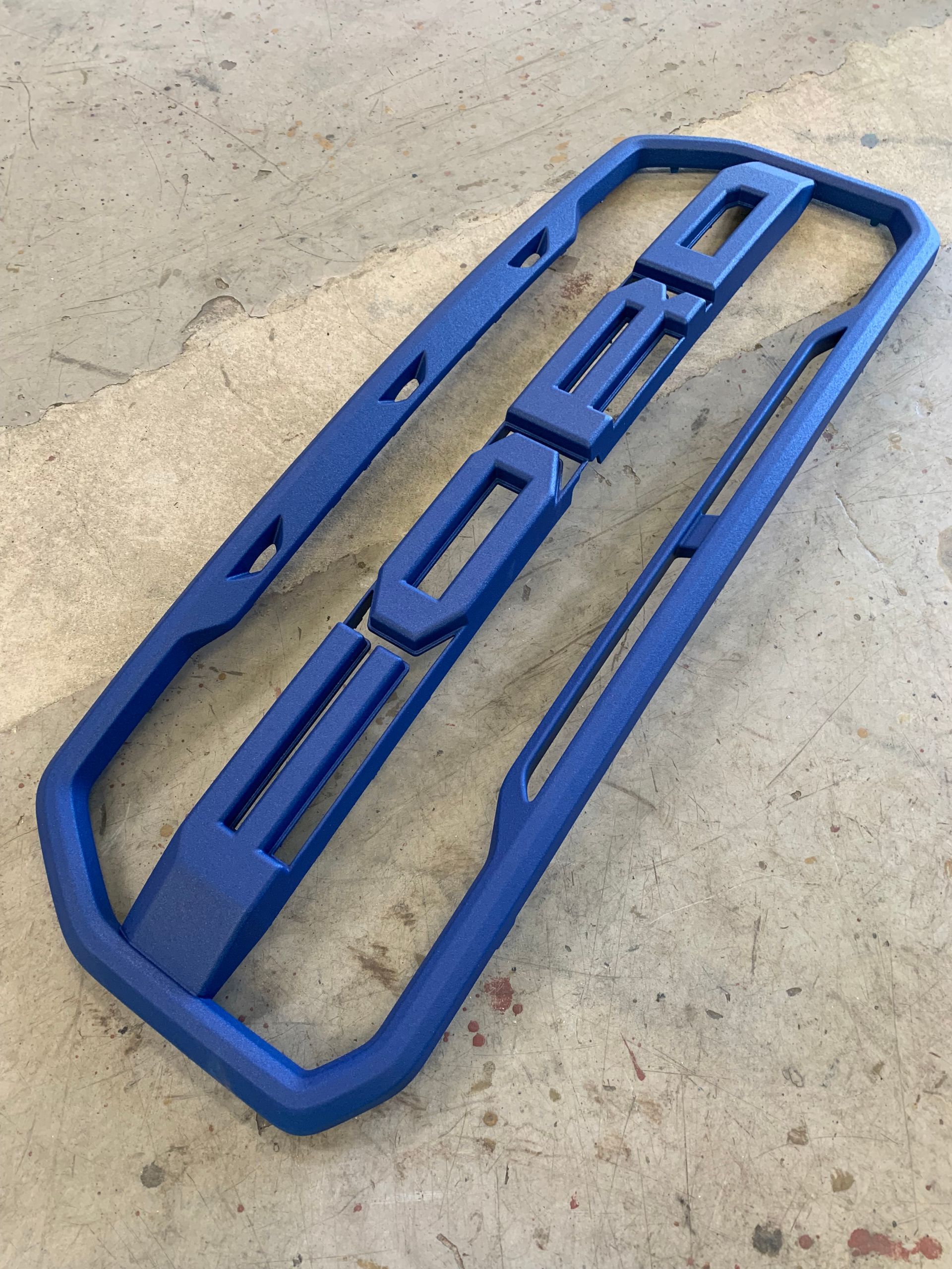 A blue, modular Ford front grille emblem assembly resting on a concrete surface.