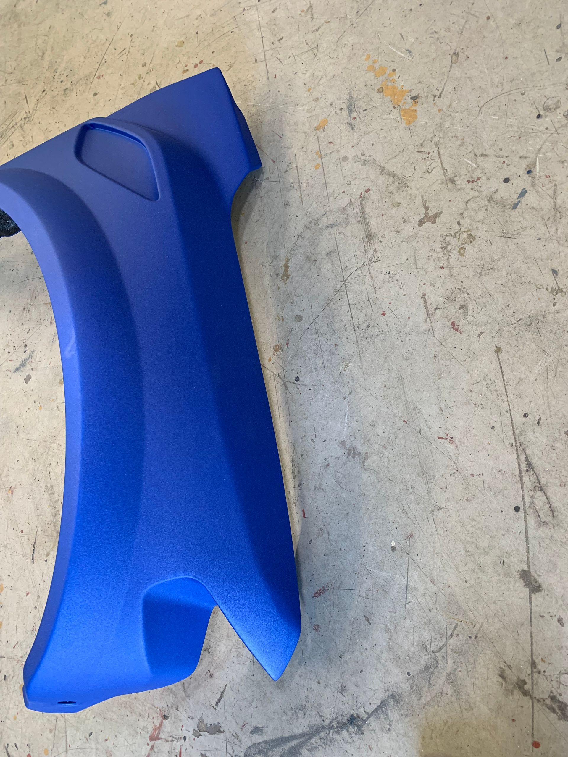 A bright blue, textured automotive fender flare resting on a concrete floor.
