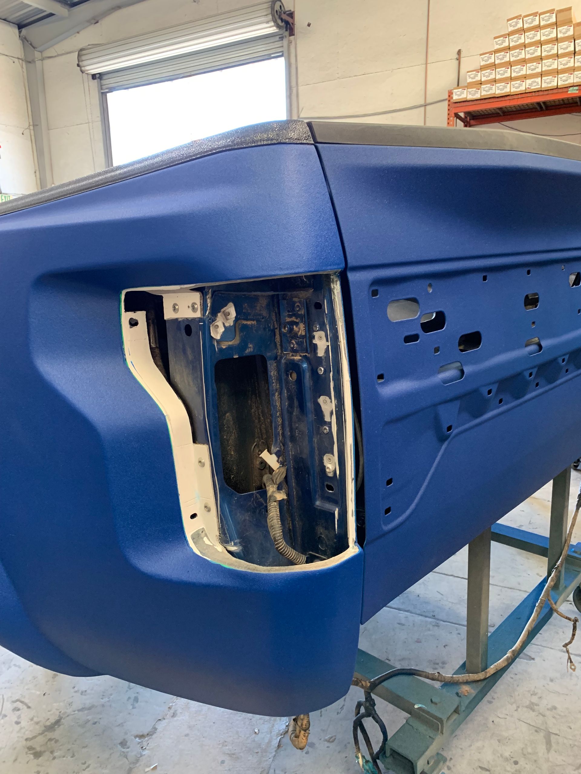 Blue truck tailgate with a textured finish, showing the rear light housing on a work stand in a garage.