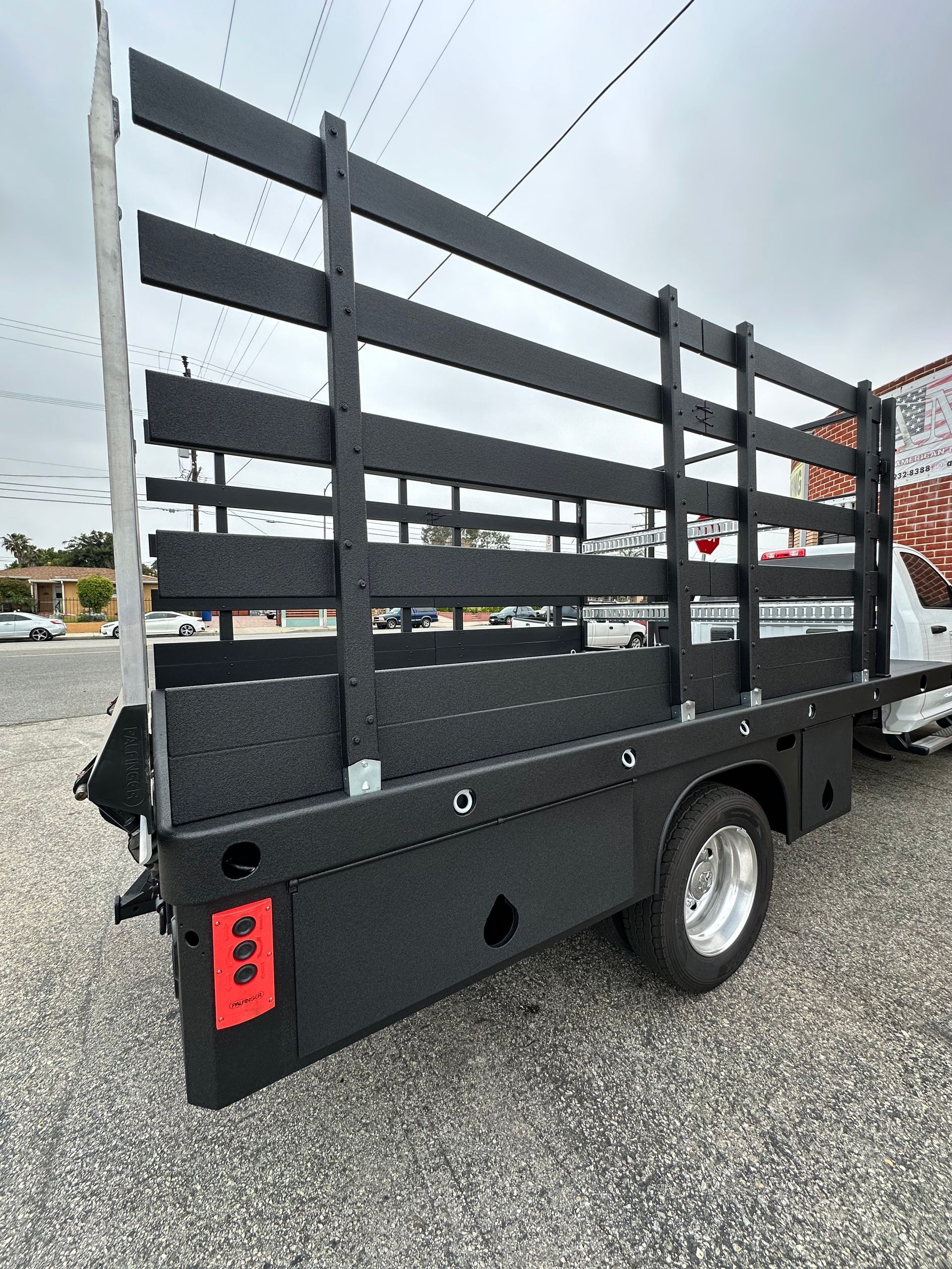 Rear view of a white truck featuring a custom-built black stake bed with high wooden side rails on a gravel lot.