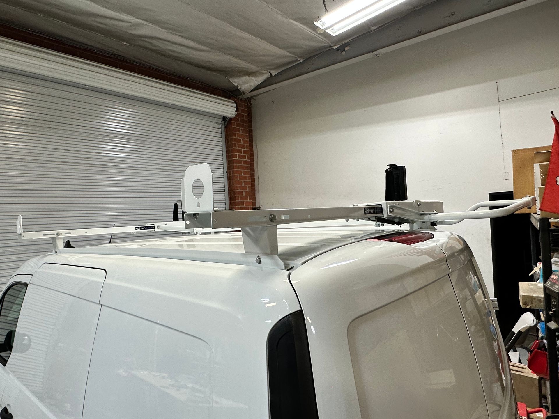 A white roof rack system mounted on top of a white van parked inside an indoor garage.