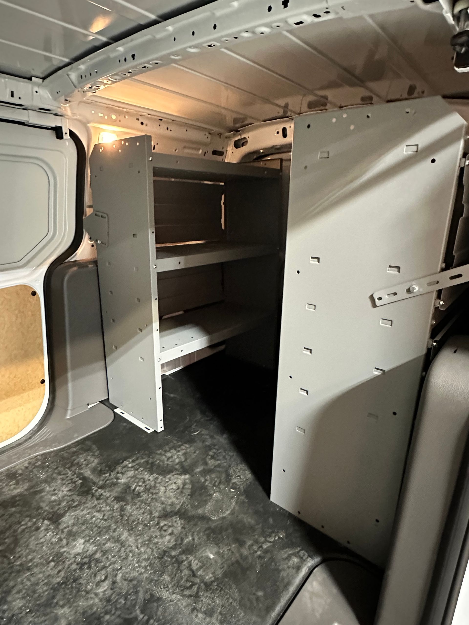 Interior of a cargo van featuring grey metal storage shelving units installed against the side wall.