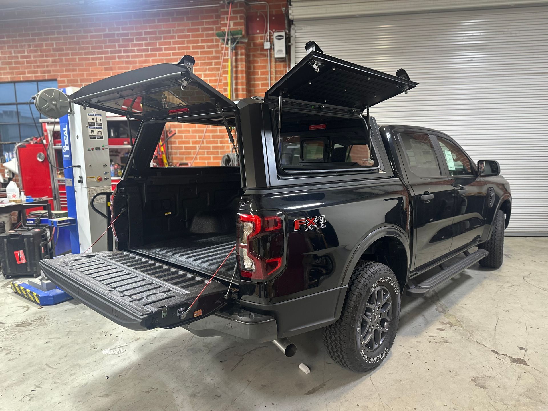 A black Ford F-150 truck with open utility camper shell side panels and tailgate, parked inside a garage.