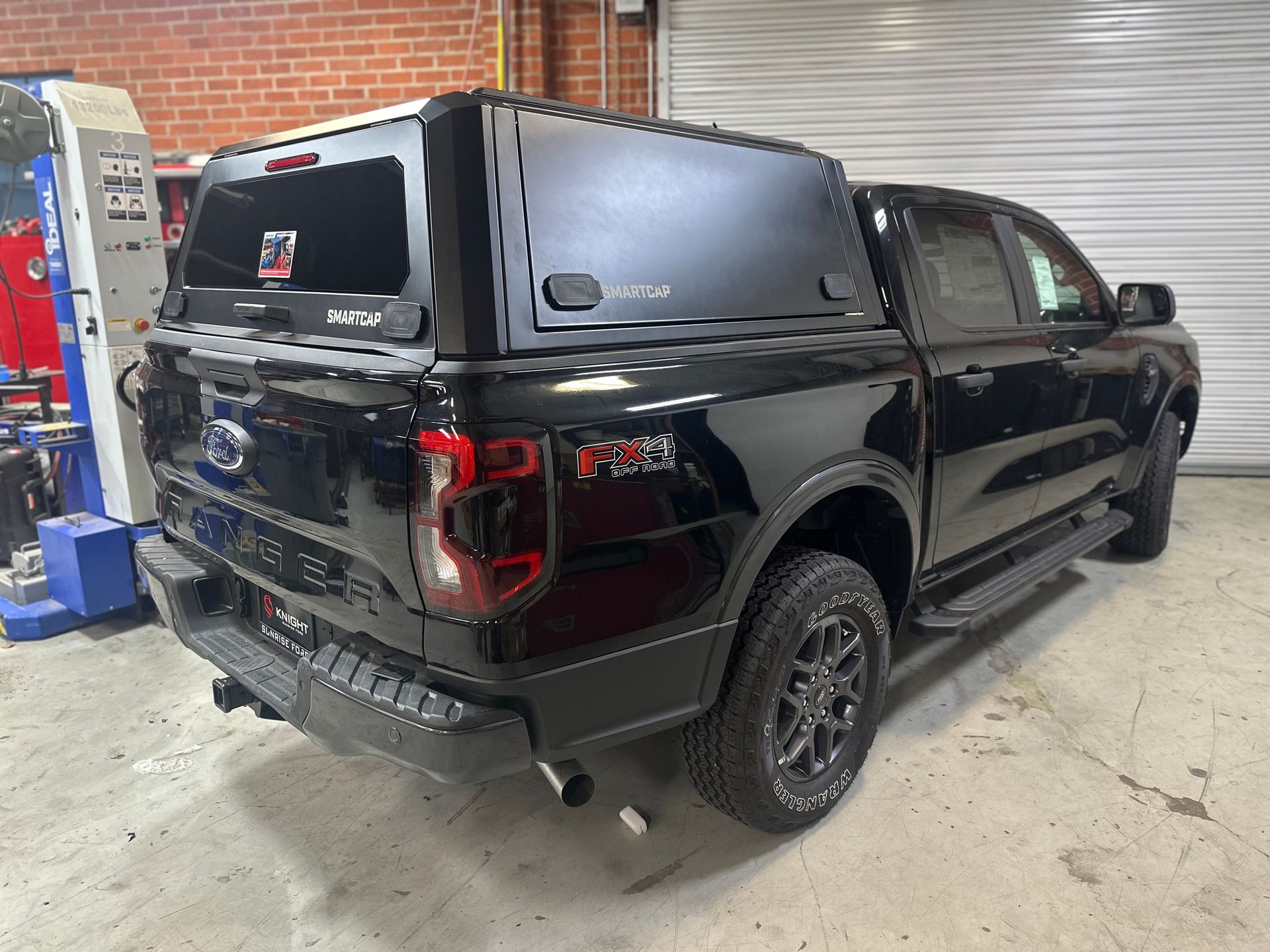 A black Ford Ranger pickup truck with a matching canopy parked in an auto garage.