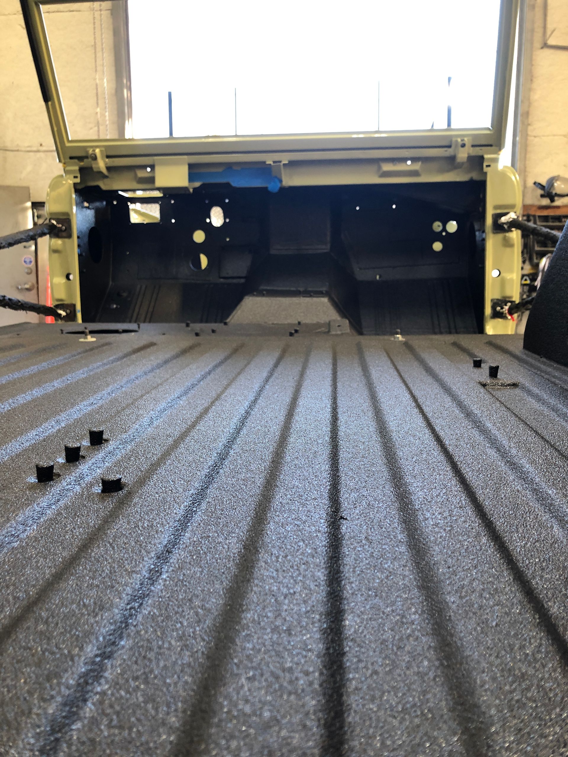 Interior view of a vehicle cargo area with a textured black bed liner, looking toward the tailgate area.