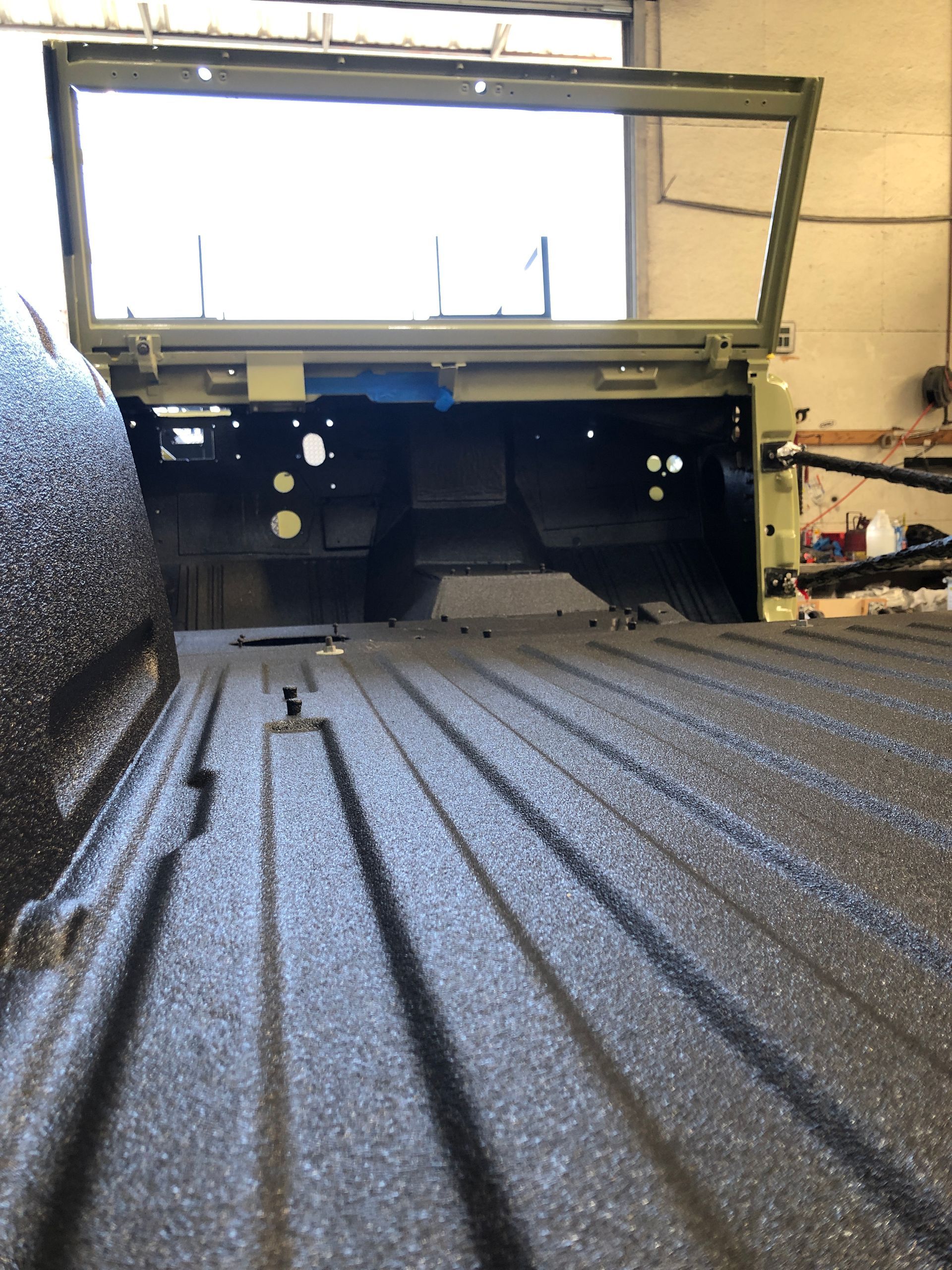 The bed of a pickup truck featuring a textured black spray-on liner, looking toward the green cab interior of the vehicle.