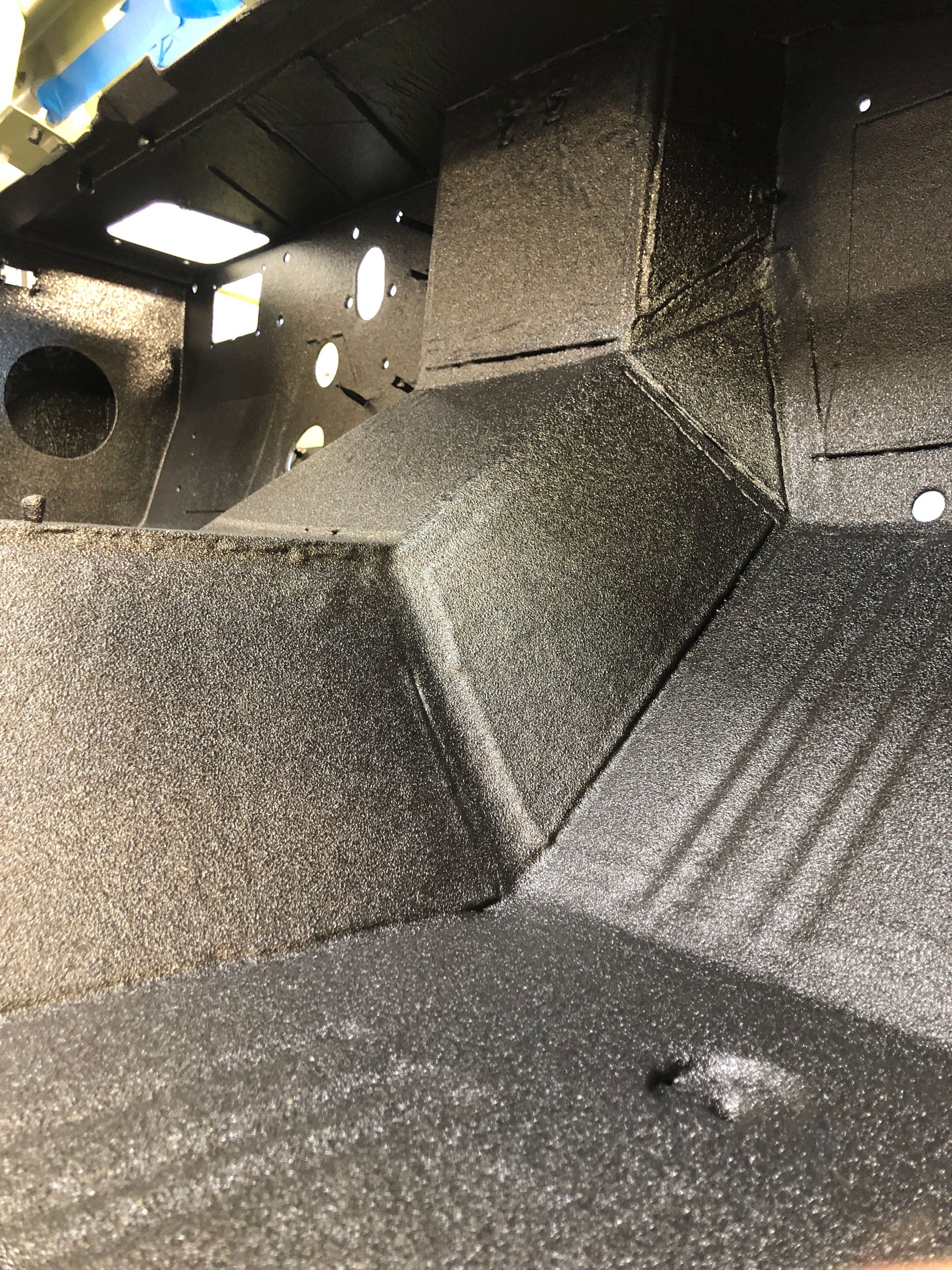 Interior of a vehicle floor covered in a textured black protective spray-on bedliner coating.