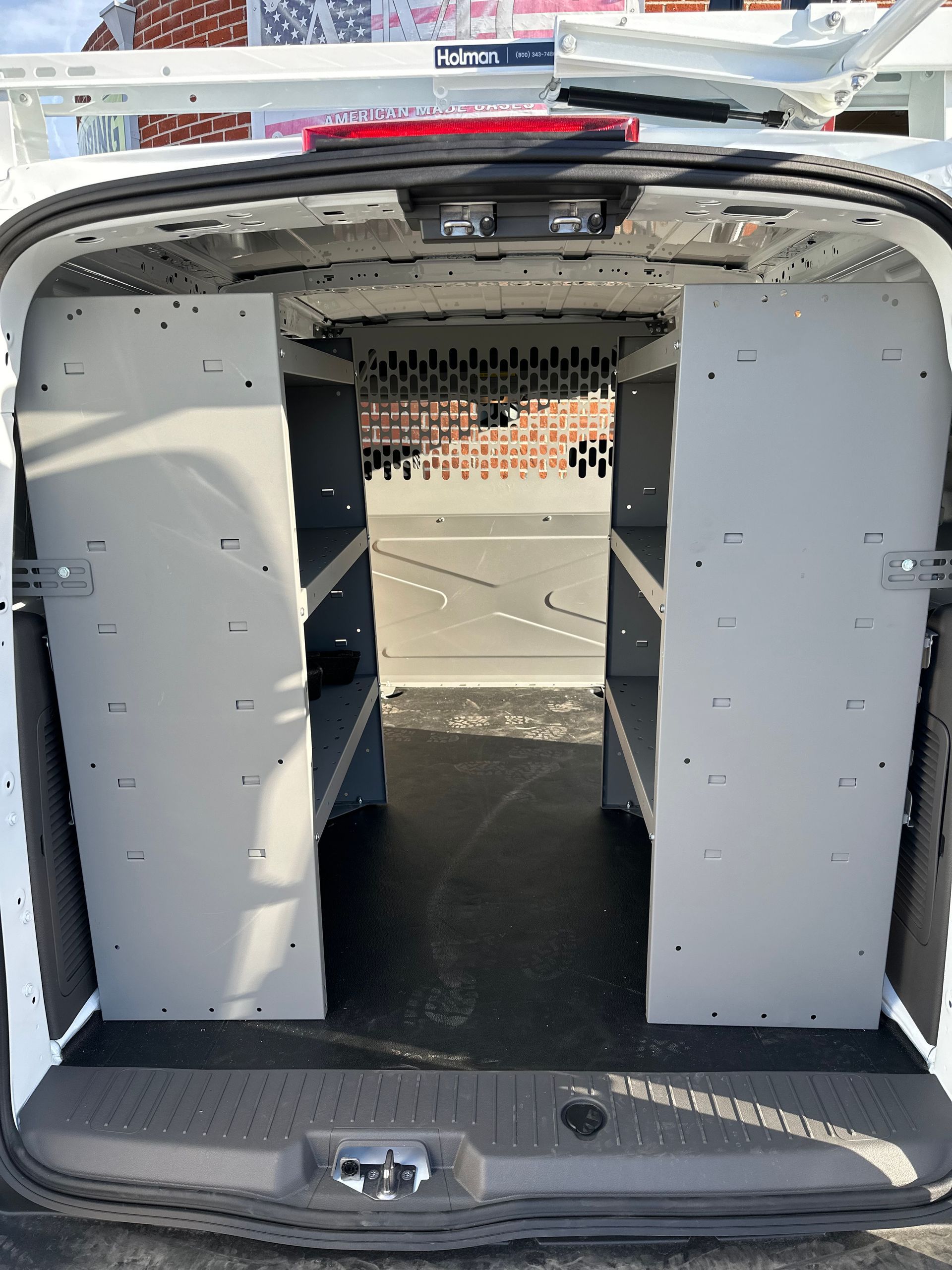 Interior view of a work van cargo area with gray metal shelving units on both sides and a dark floor.