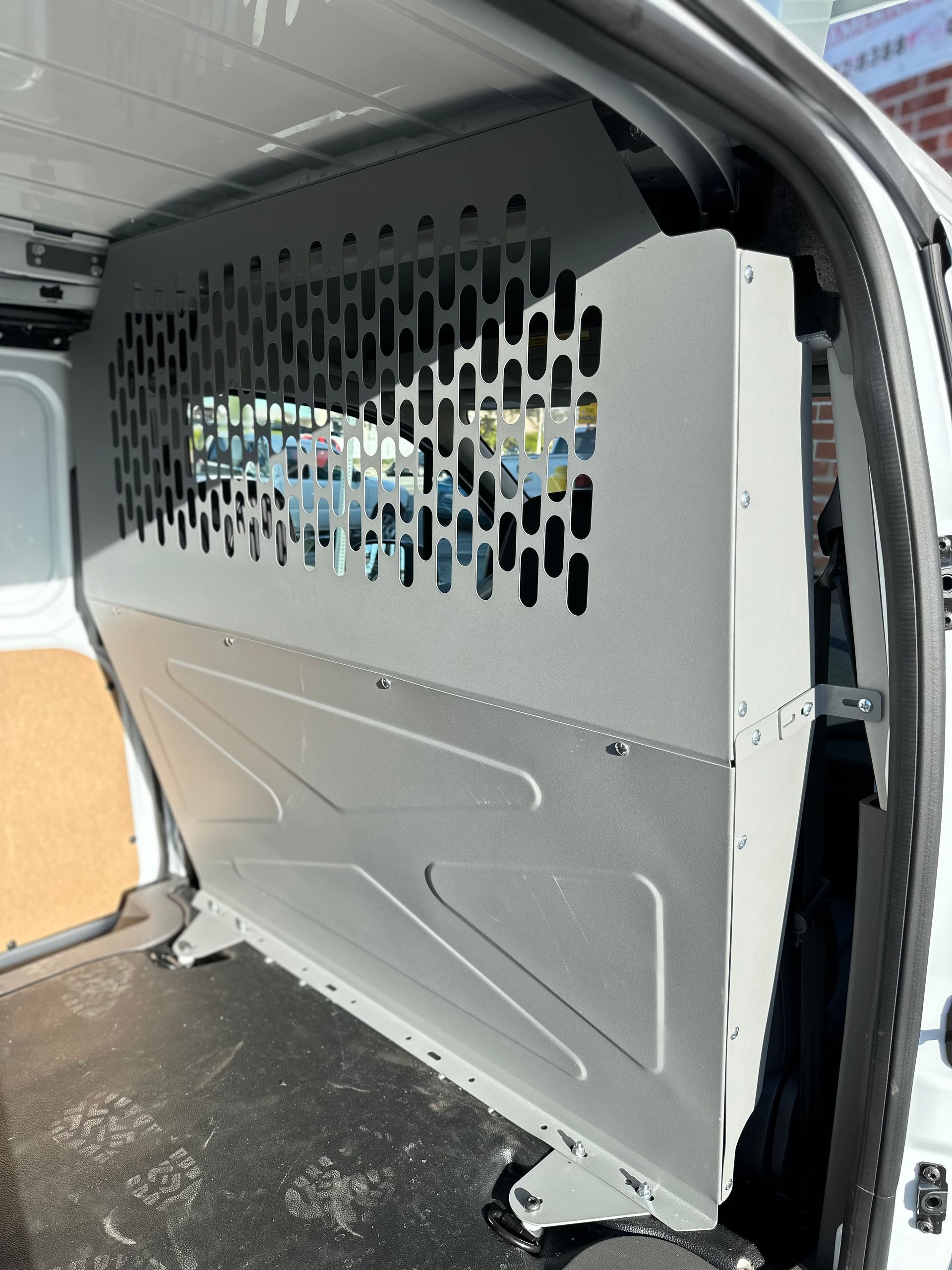 A gray metal security partition installed inside the cargo area of a white commercial van.