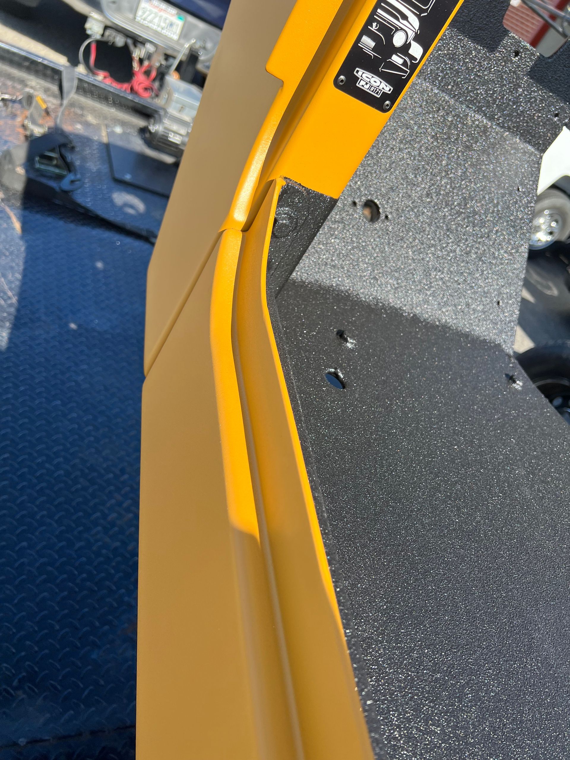 A close-up of a yellow metal edge with textured black grip tape on a piece of heavy machinery or equipment.