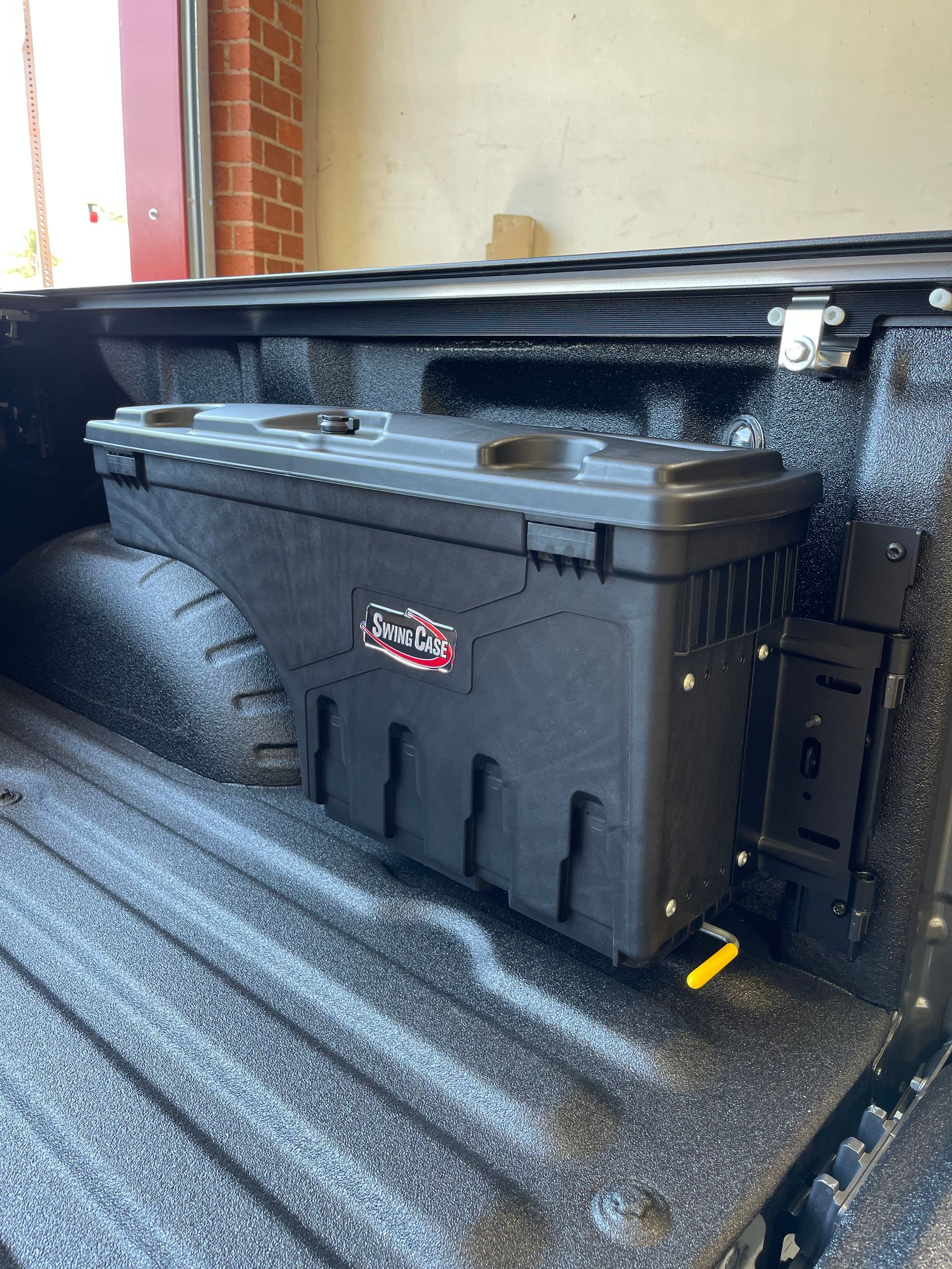 A black Swing Case truck bed storage box mounted on the side wall of a black pickup truck bed.