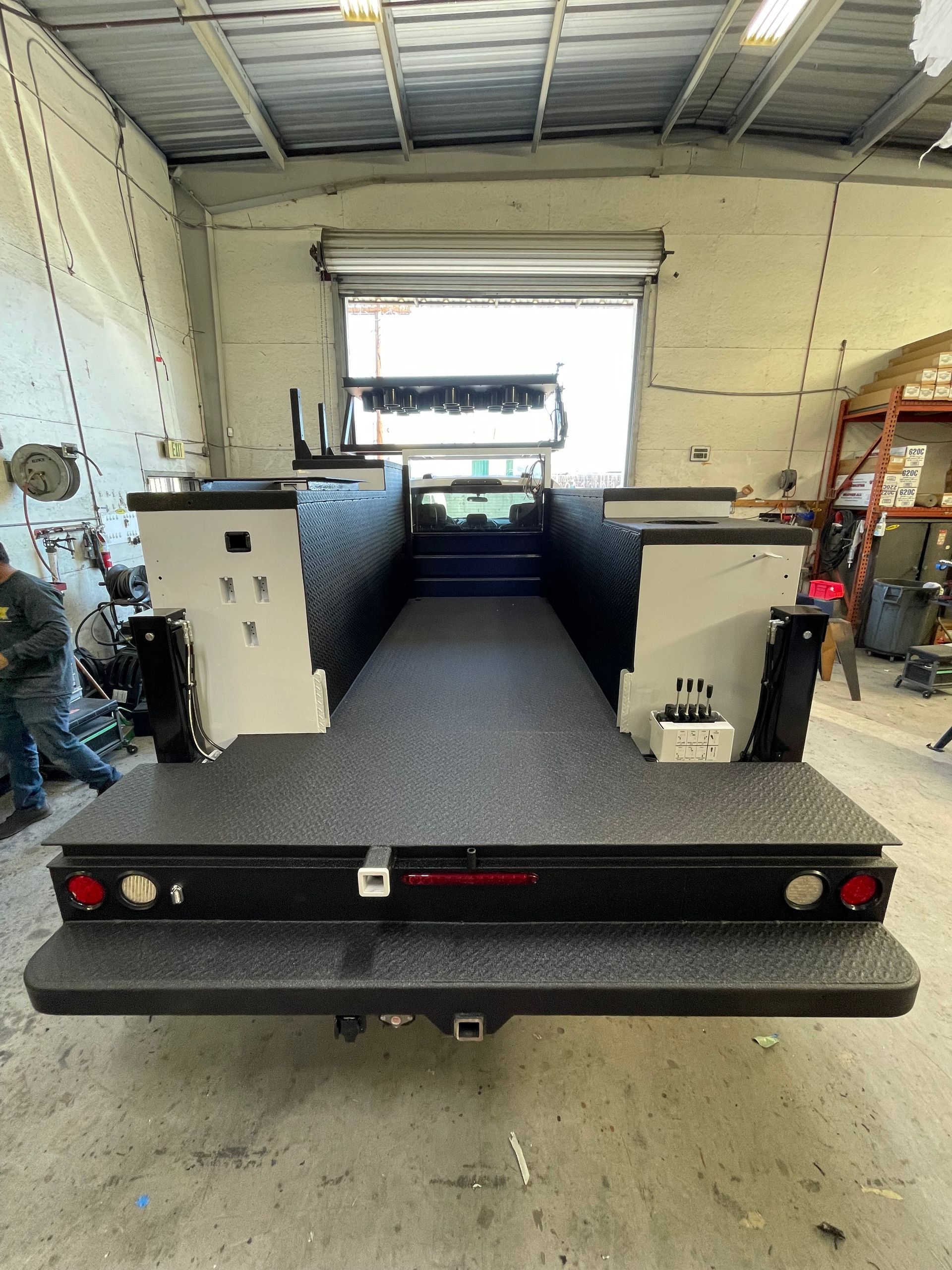 The rear view of a truck with a flatbed utility bed featuring a black diamond-plate surface, parked inside a garage.