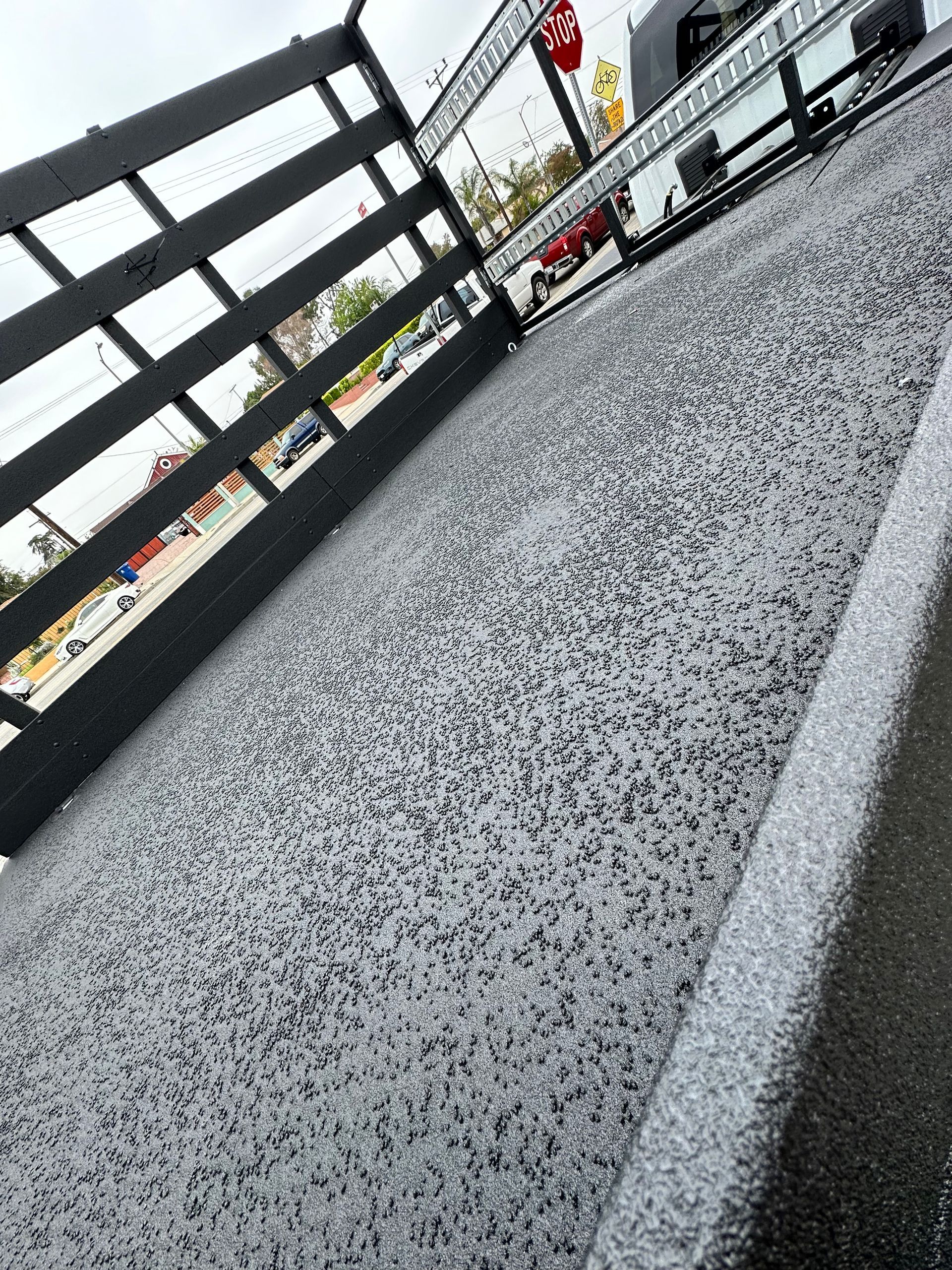 A close-up view of a grey and black speckled epoxy floor coating next to a black wooden railing outdoors.