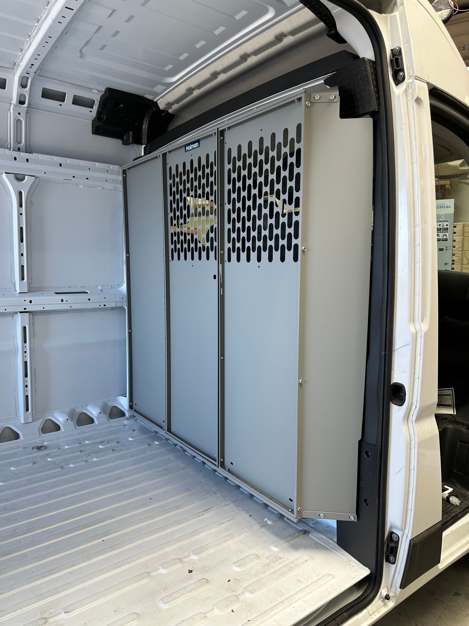 A grey metal security partition installed inside the cargo area of a white commercial van.