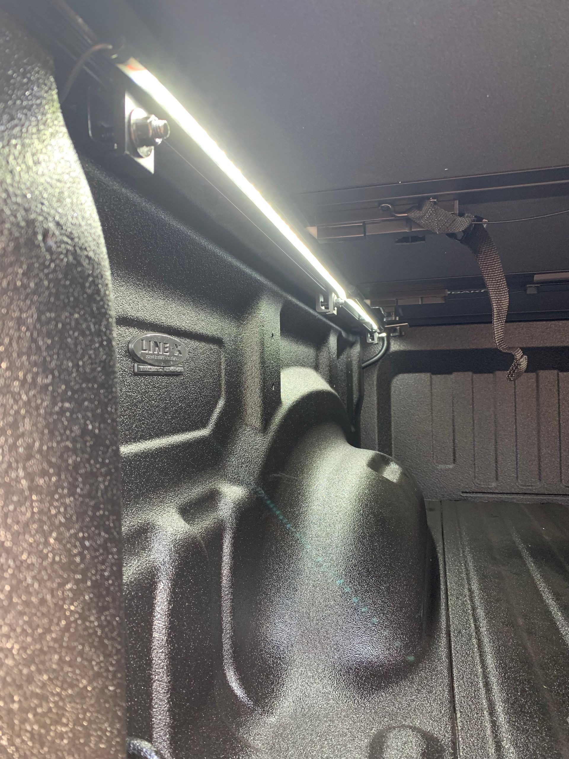 A bright LED light strip mounted along the textured, black-coated interior wall of a pickup truck cargo bed.