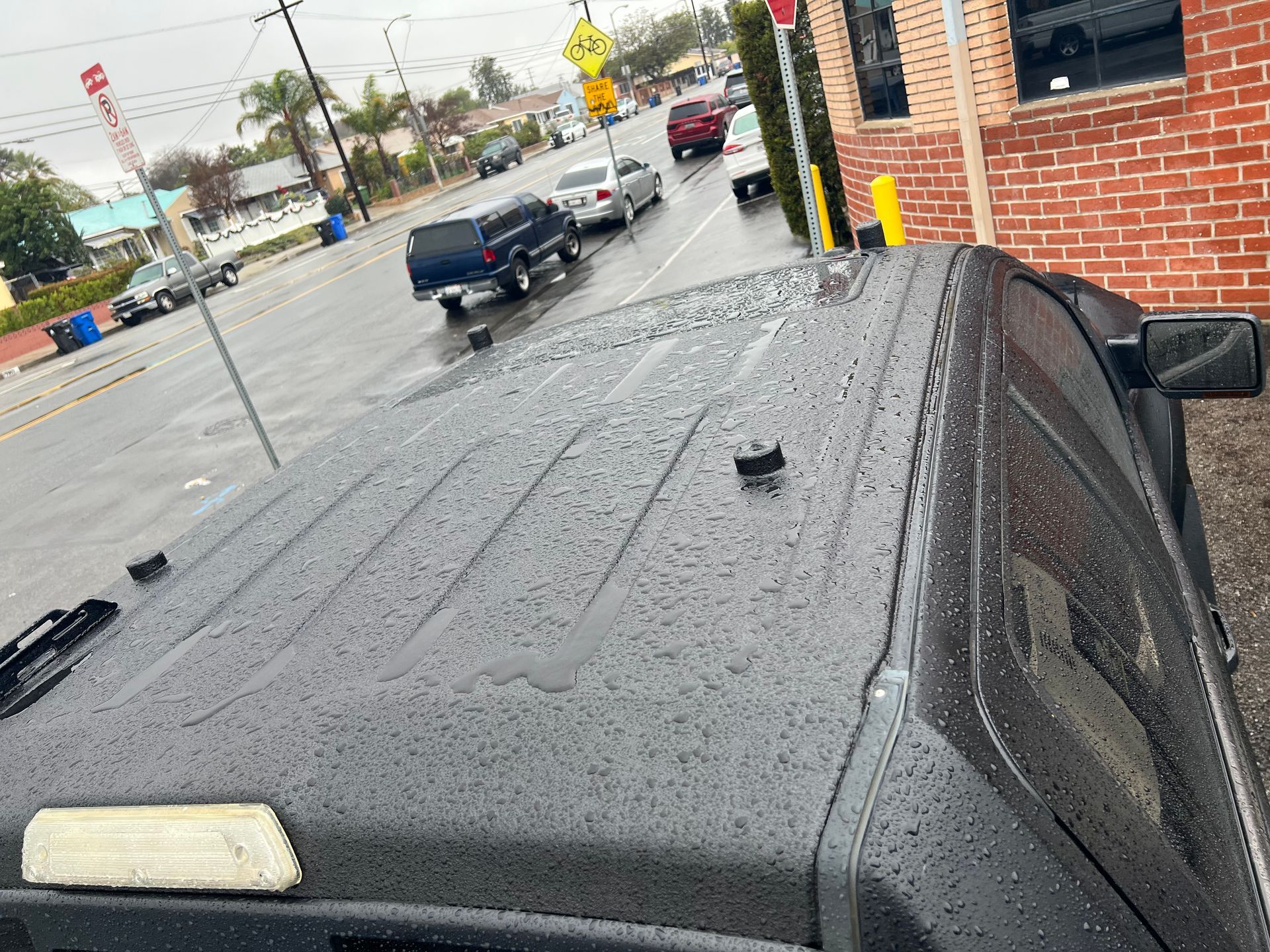 A high-angle view of a rain-covered black truck roof with a red brick building and street traffic in the background.