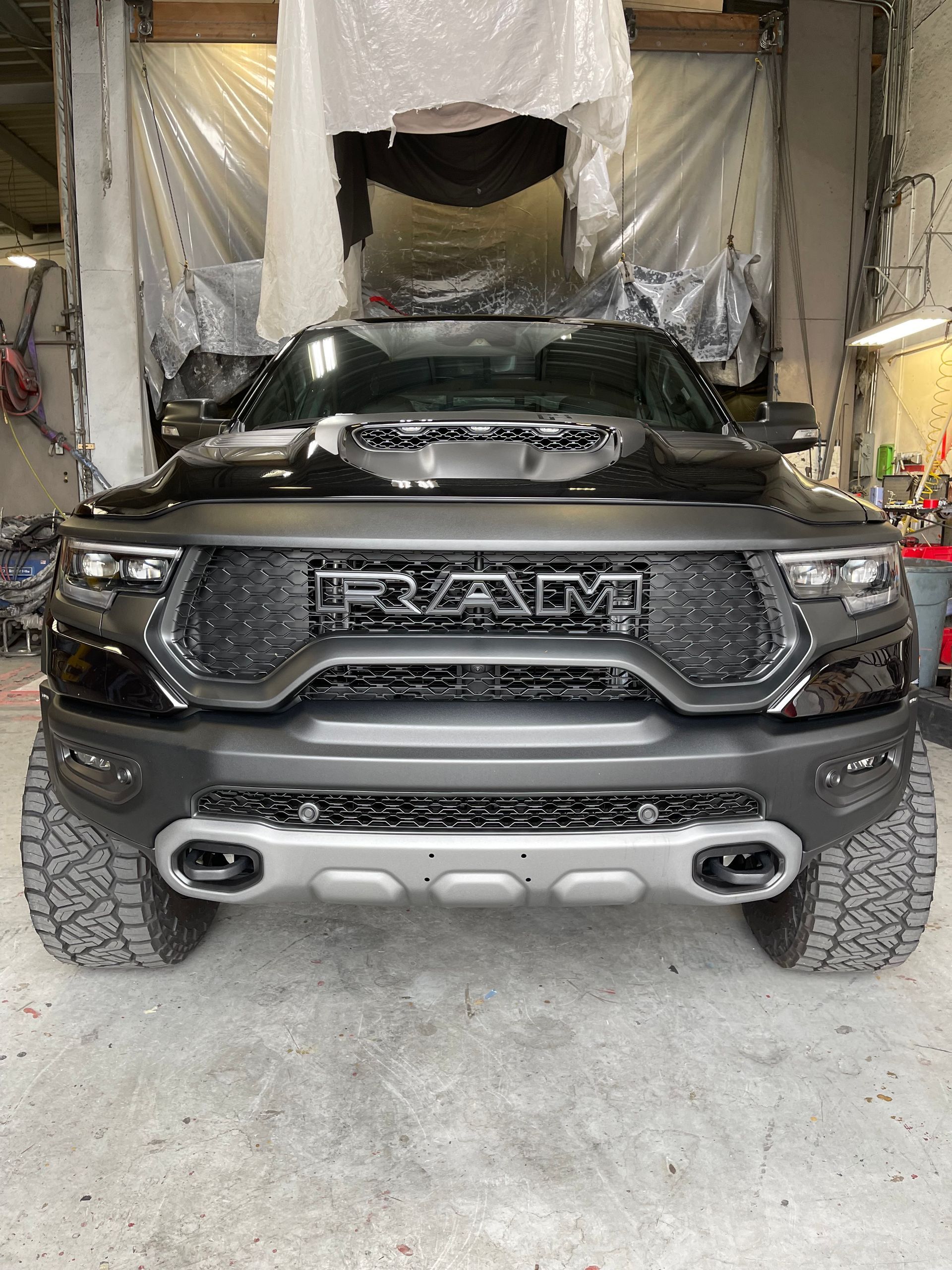 Front view of a black RAM TRX pickup truck parked inside a garage, featuring off-road tires and a metallic skid plate.