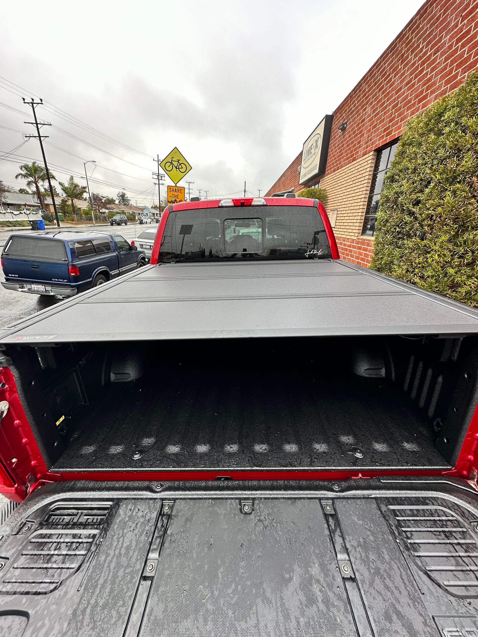 A red pickup truck with an open tailgate, showcasing a black truck bed liner and a folded tonneau cover.