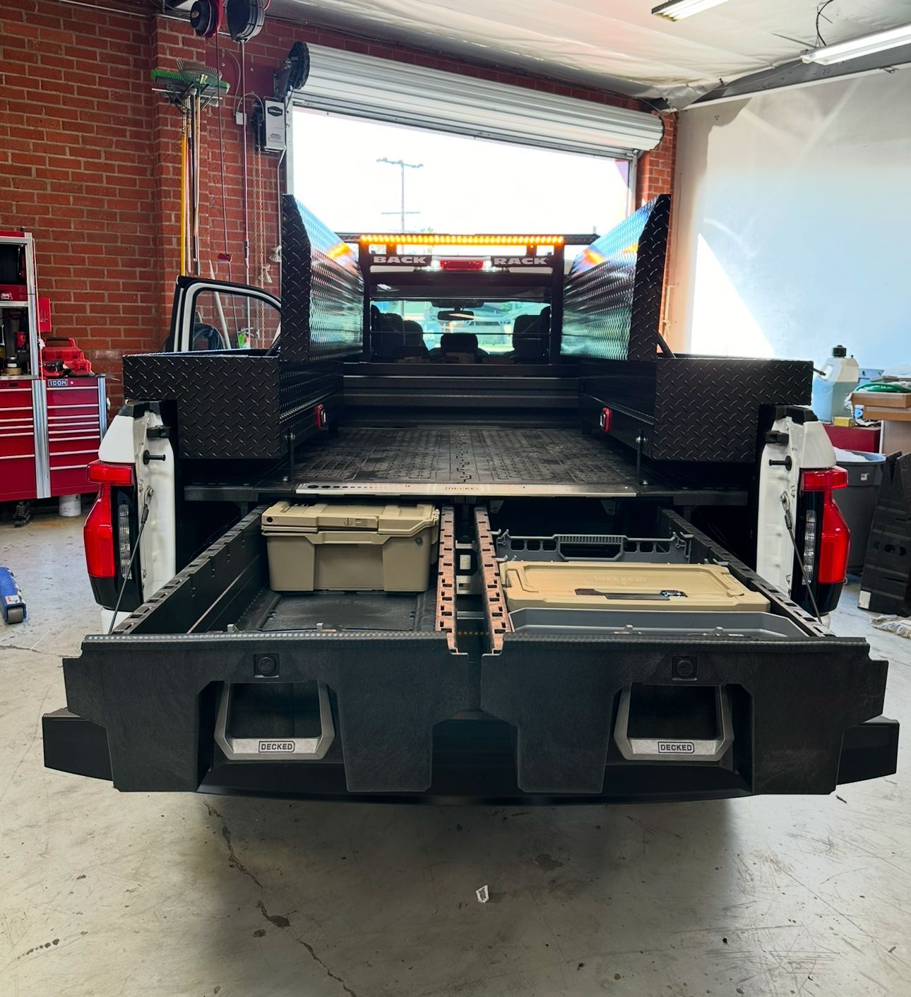 Open truck bed with a black storage drawer system installed, showing two open drawers holding gear in a garage setting.