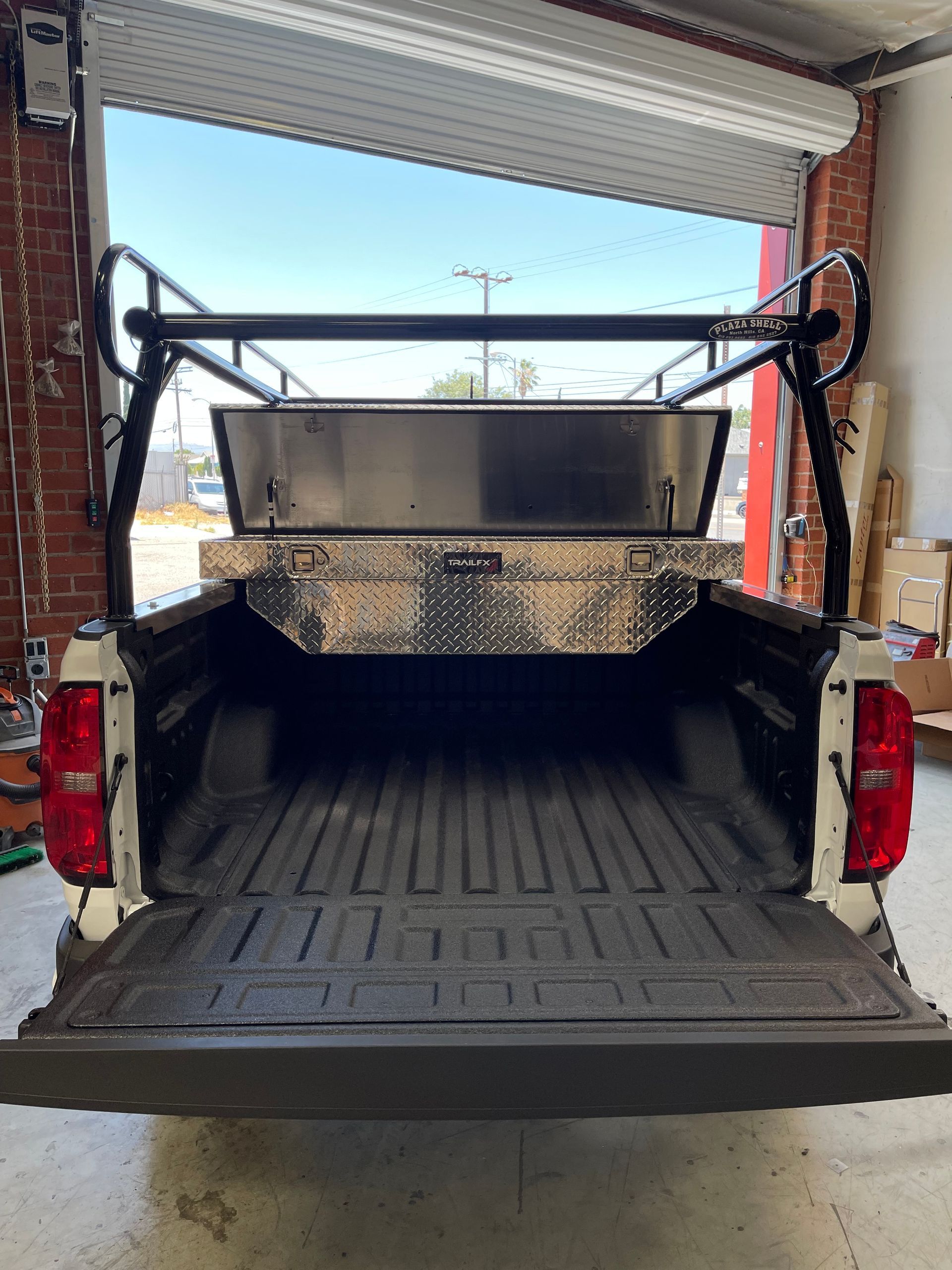 The open bed of a white pickup truck, featuring a diamond-plate metal toolbox and a black overhead cargo rack.