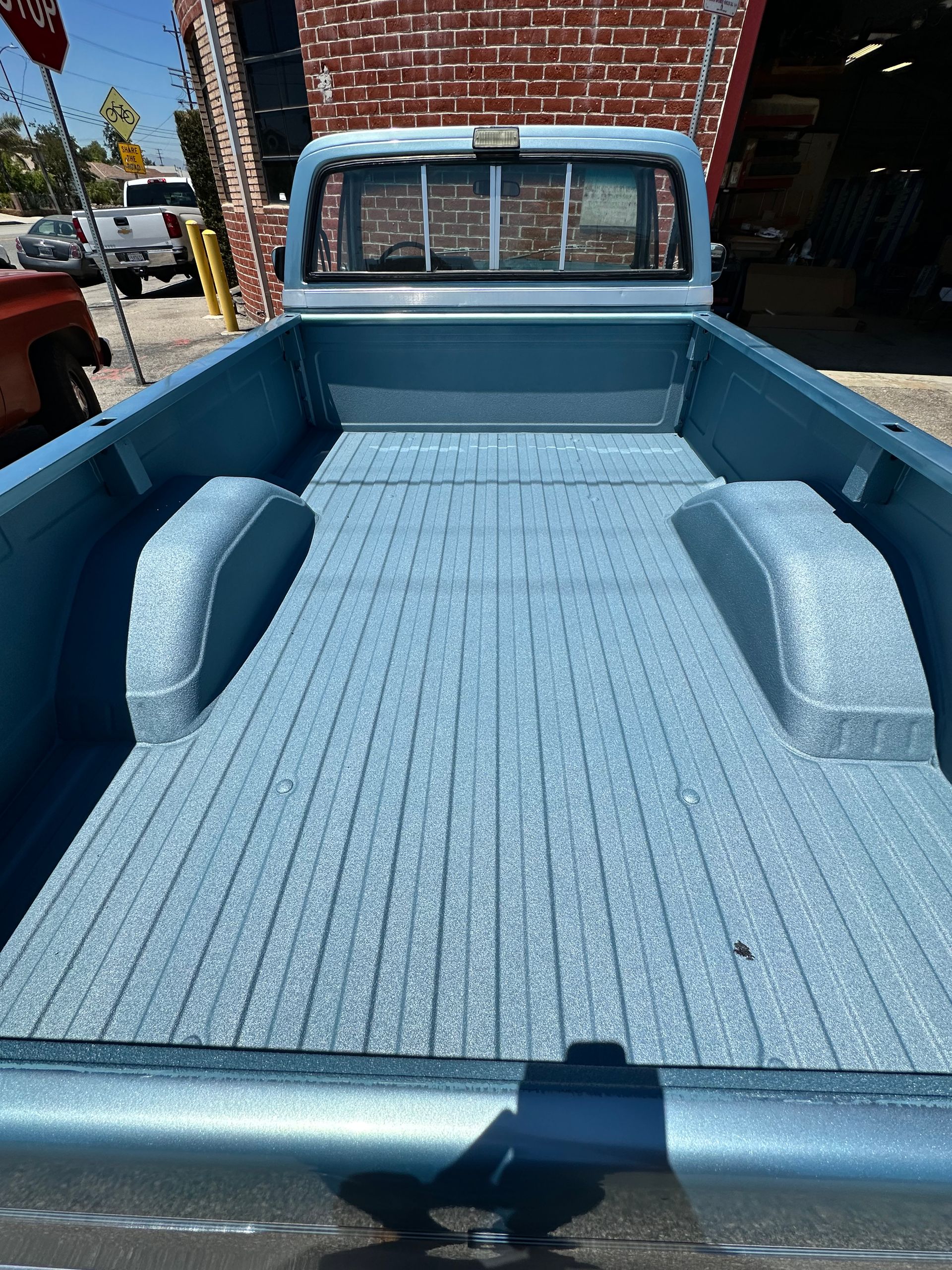 The bed of a light blue vintage pickup truck featuring a matching blue textured spray-in bed liner.