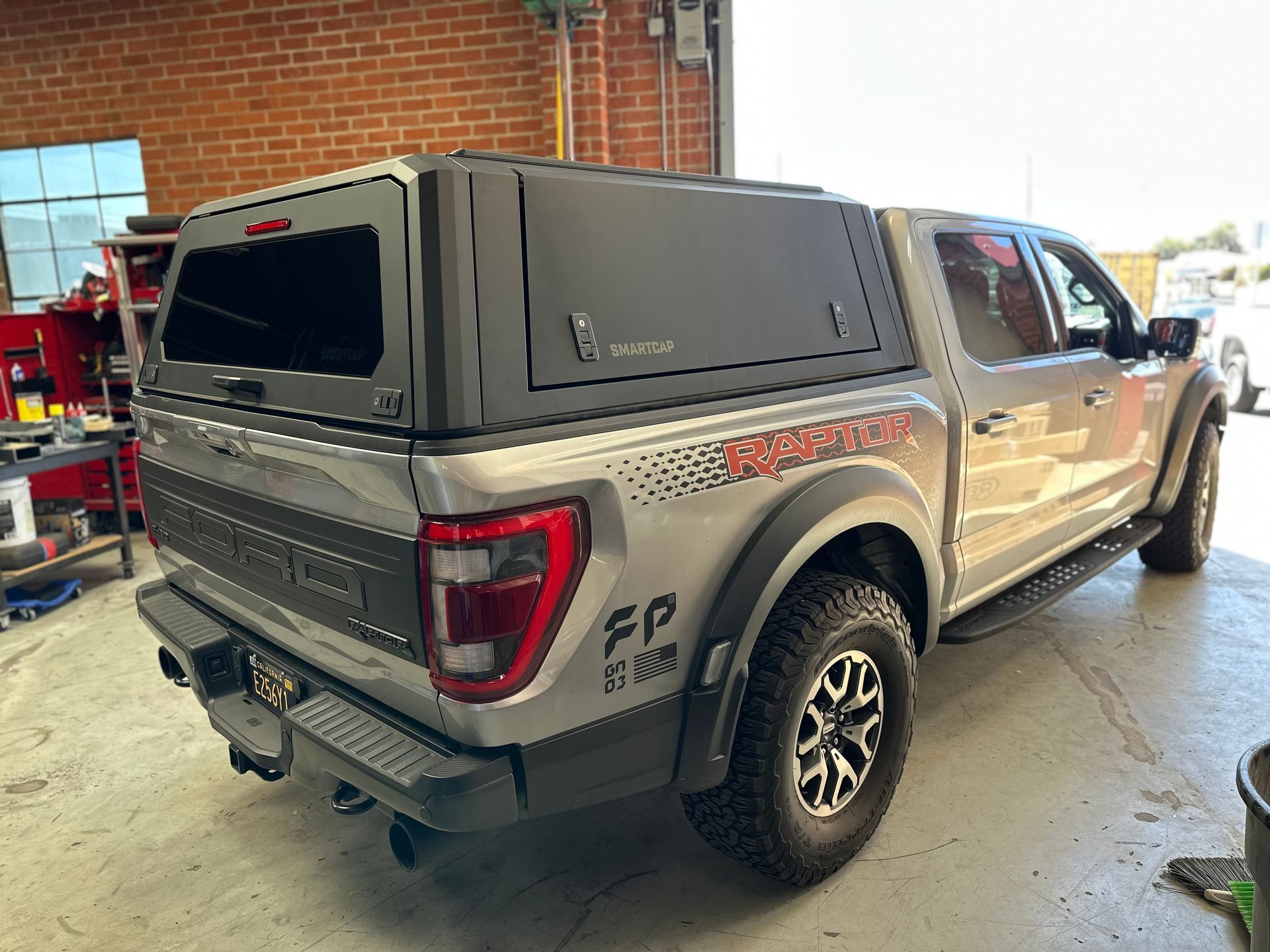 A silver Ford Raptor pickup truck with a black camper shell parked inside a garage.