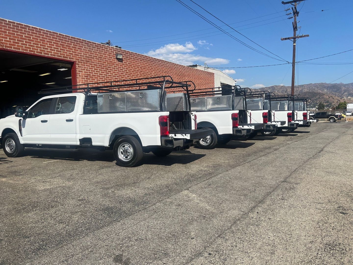 White work trucks parked in a row outside a brick building on a sunny day.