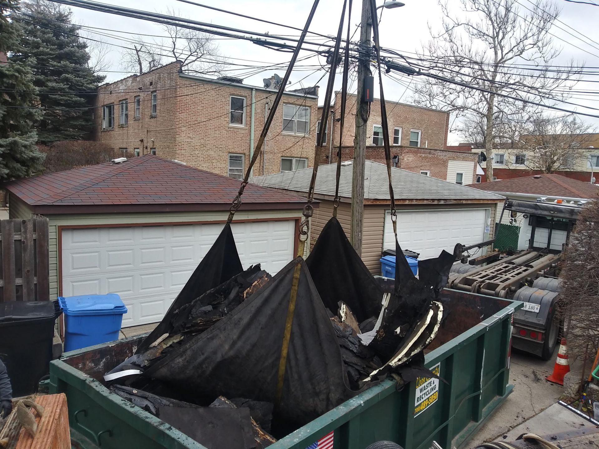 A dumpster filled with junk is being lifted by a crane.