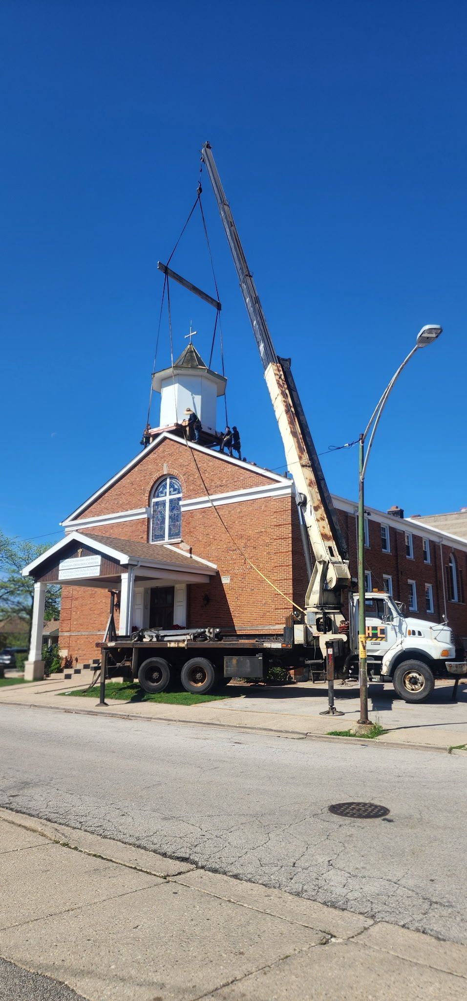 A truck with a crane attached to it is parked in front of a brick church.