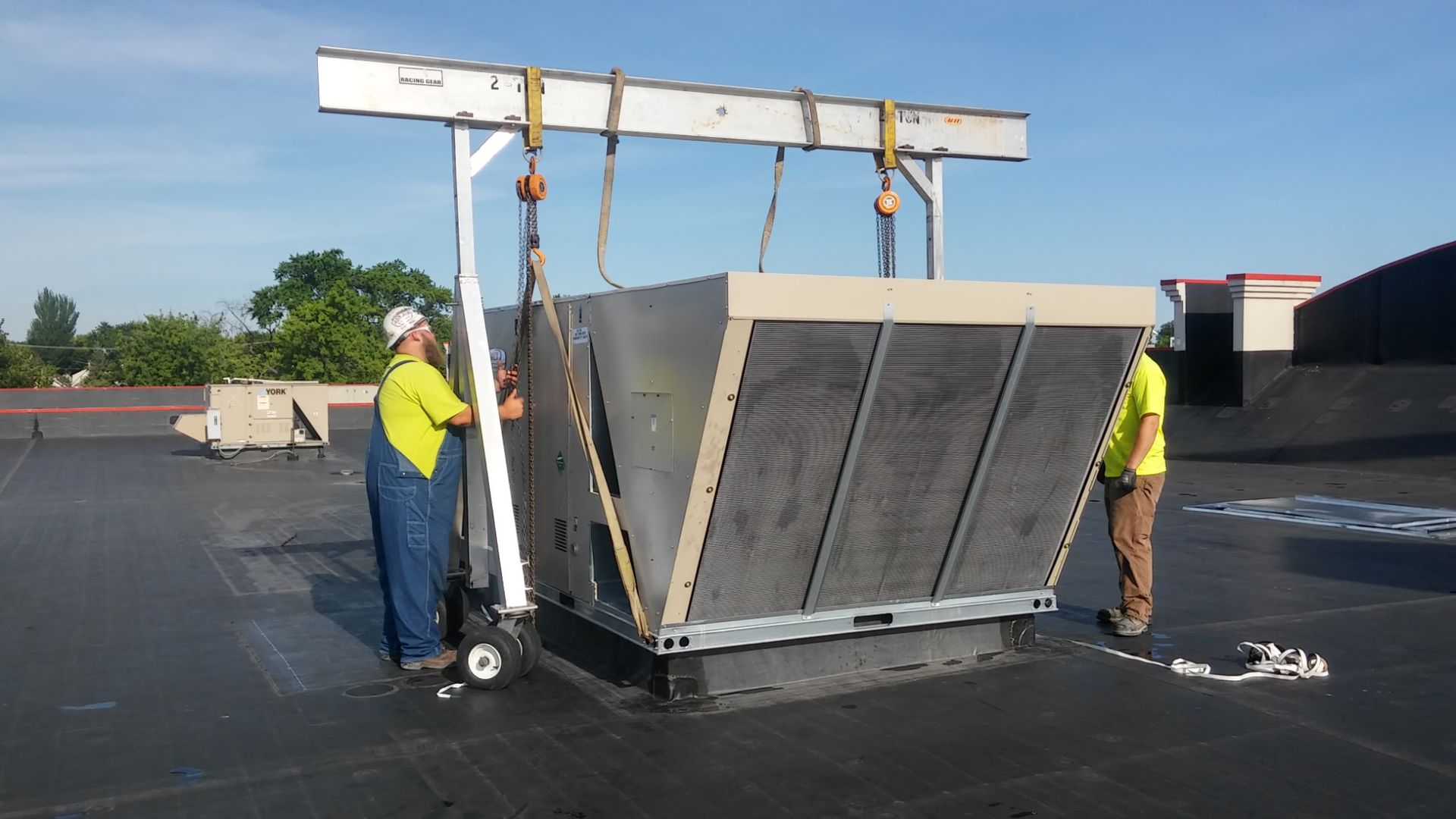 Two men are working on a large piece of equipment on a roof.